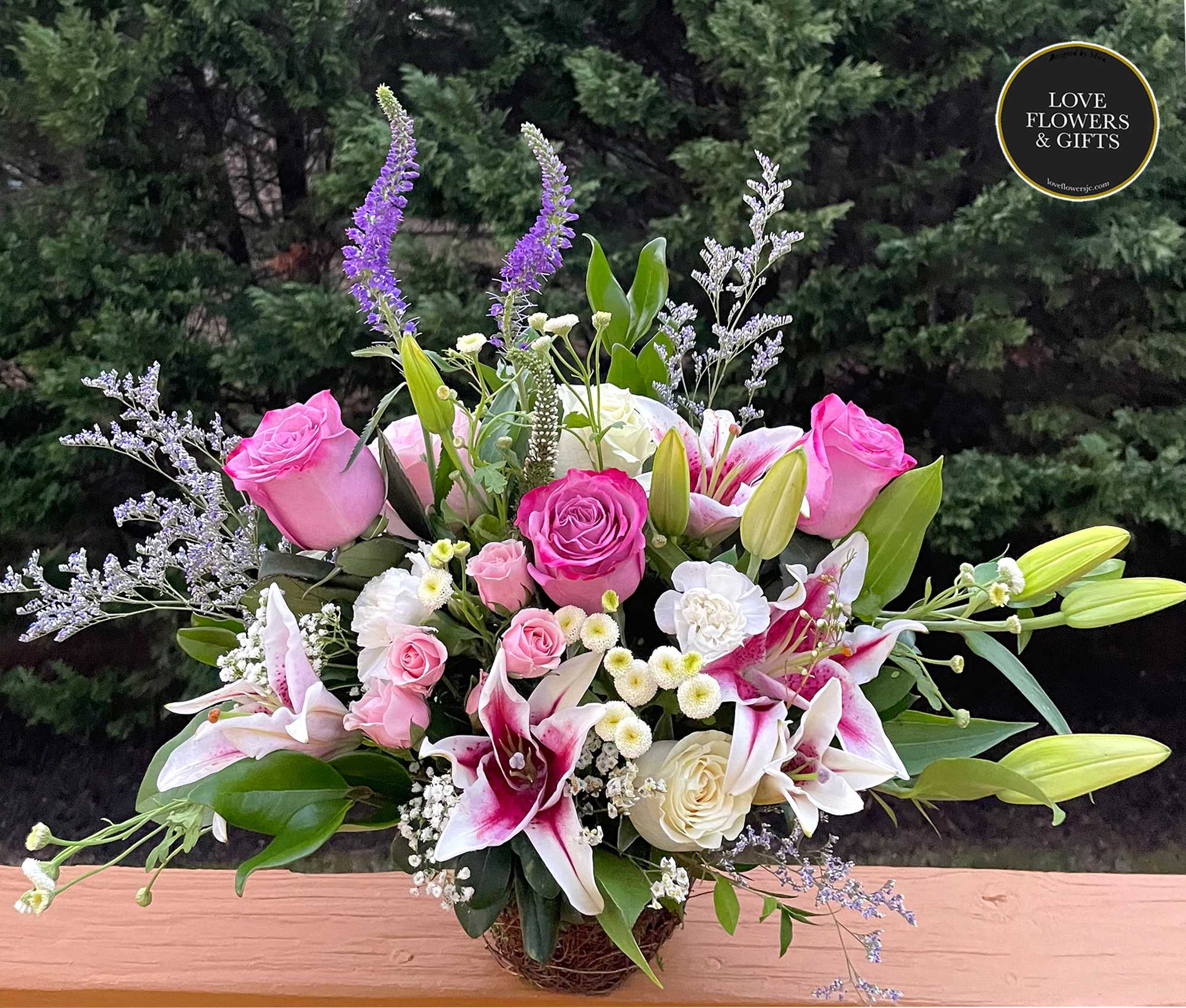 Pink roses and white lilies with accent blooms arranged in a low glass vase