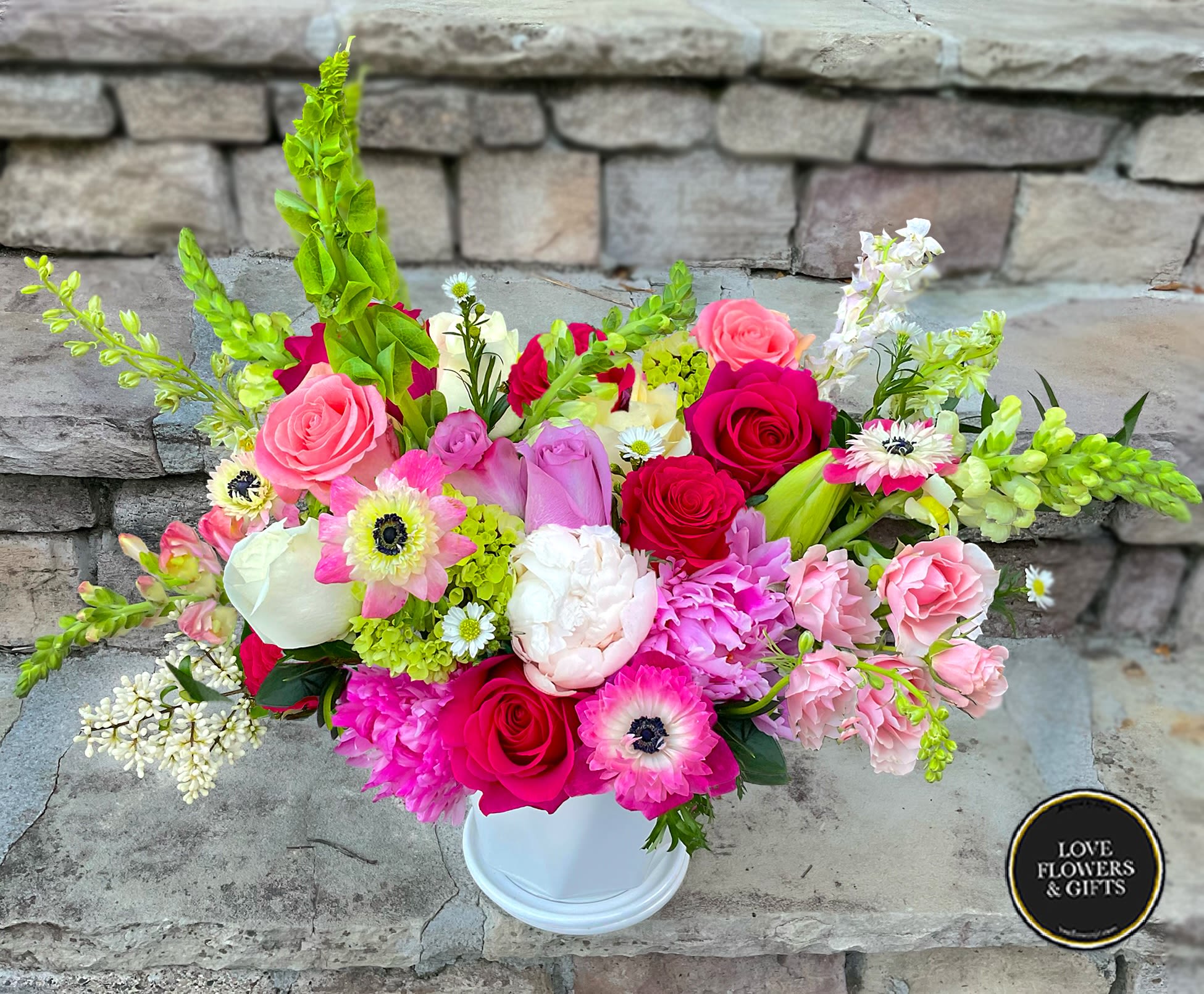 Low white vase filled with pink roses, peonies, anemones and mixed blooms on stone steps