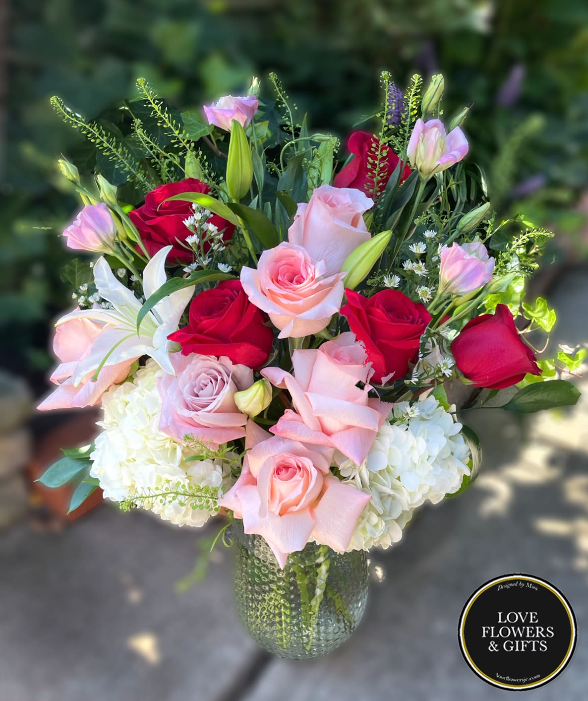 Arrangement of red and pink roses with white lilies and hydrangeas in a textured glass vase