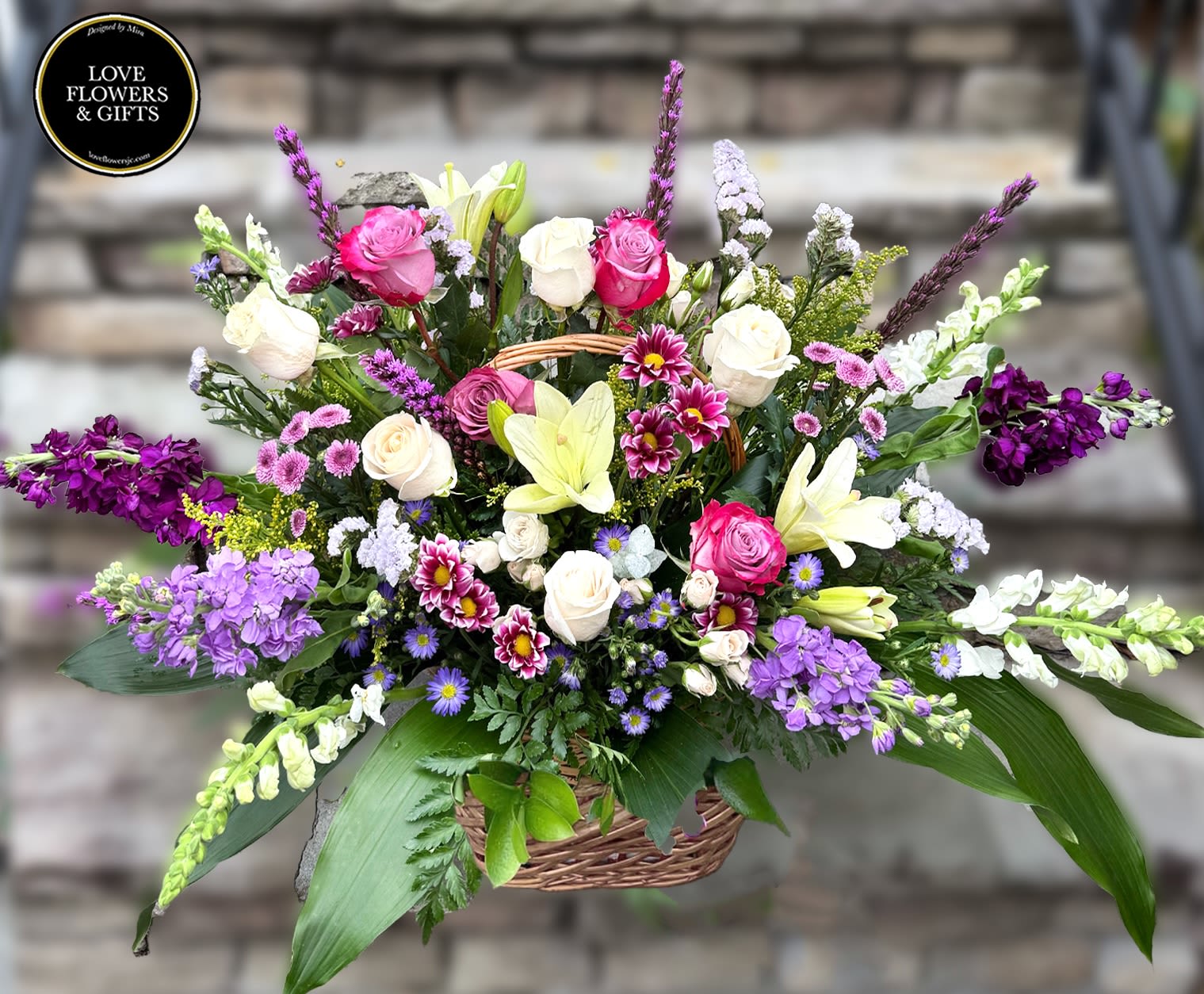 Large mixed basket arrangement with pink and white roses, lilies, and purple accent flowers.