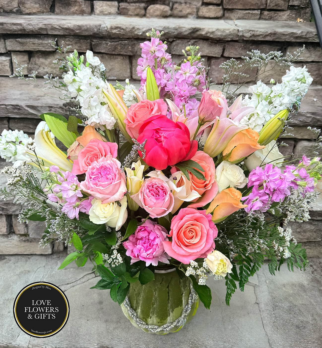 Peony Rush  - A grand spring summer arrangement with peonies and mixed blooms in a decortaed green frosted glass vase. 