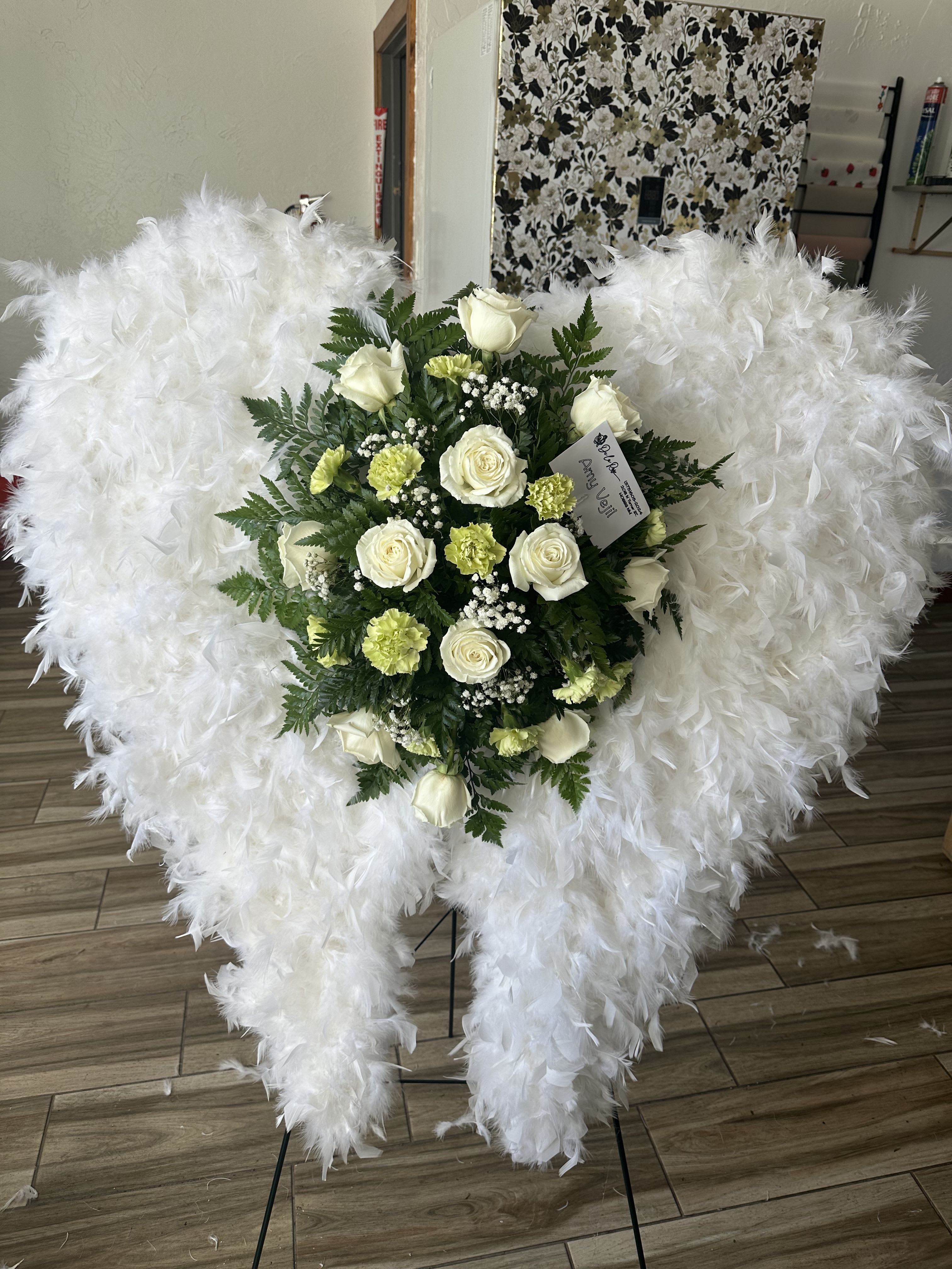 Angelic Serenity - This floral angelic funeral spray is an everlasting tribute to that someone special.   Includes: white roses, light green carnations, greenery, and fluffy angel wings. 