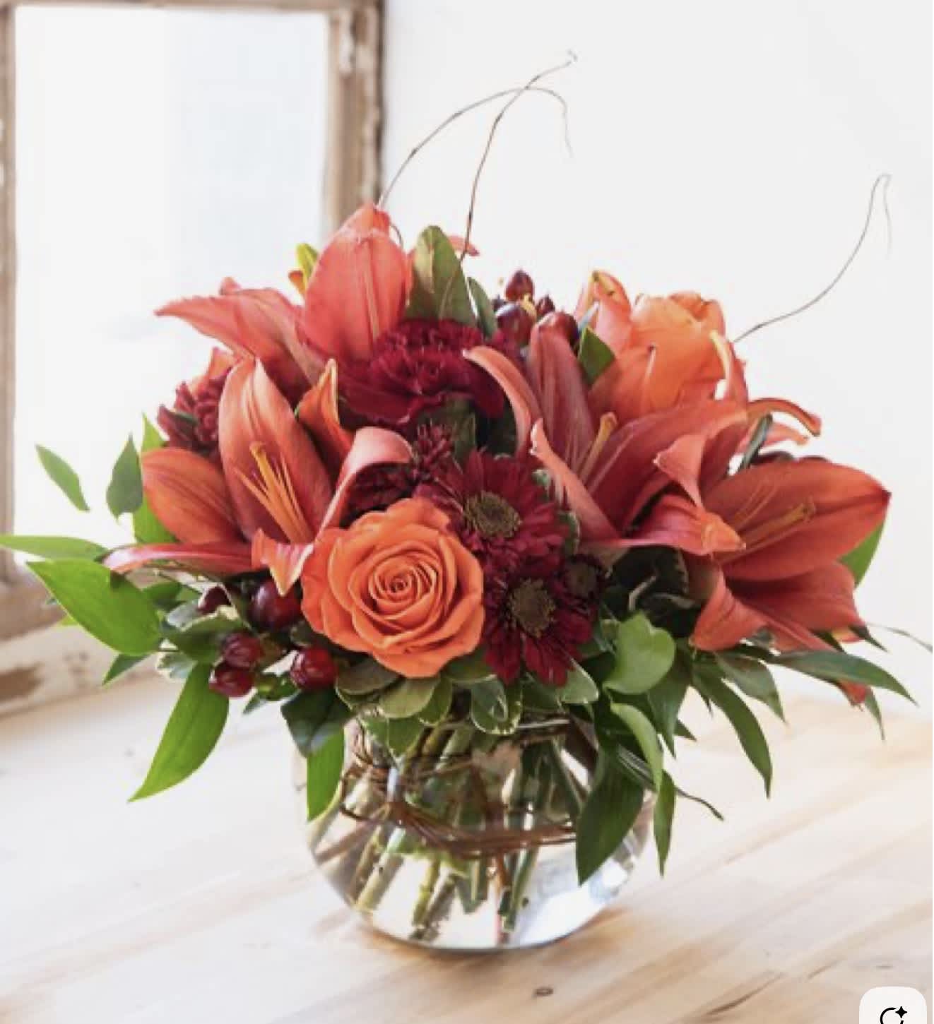 Orange lilies and roses in a clear glass vase