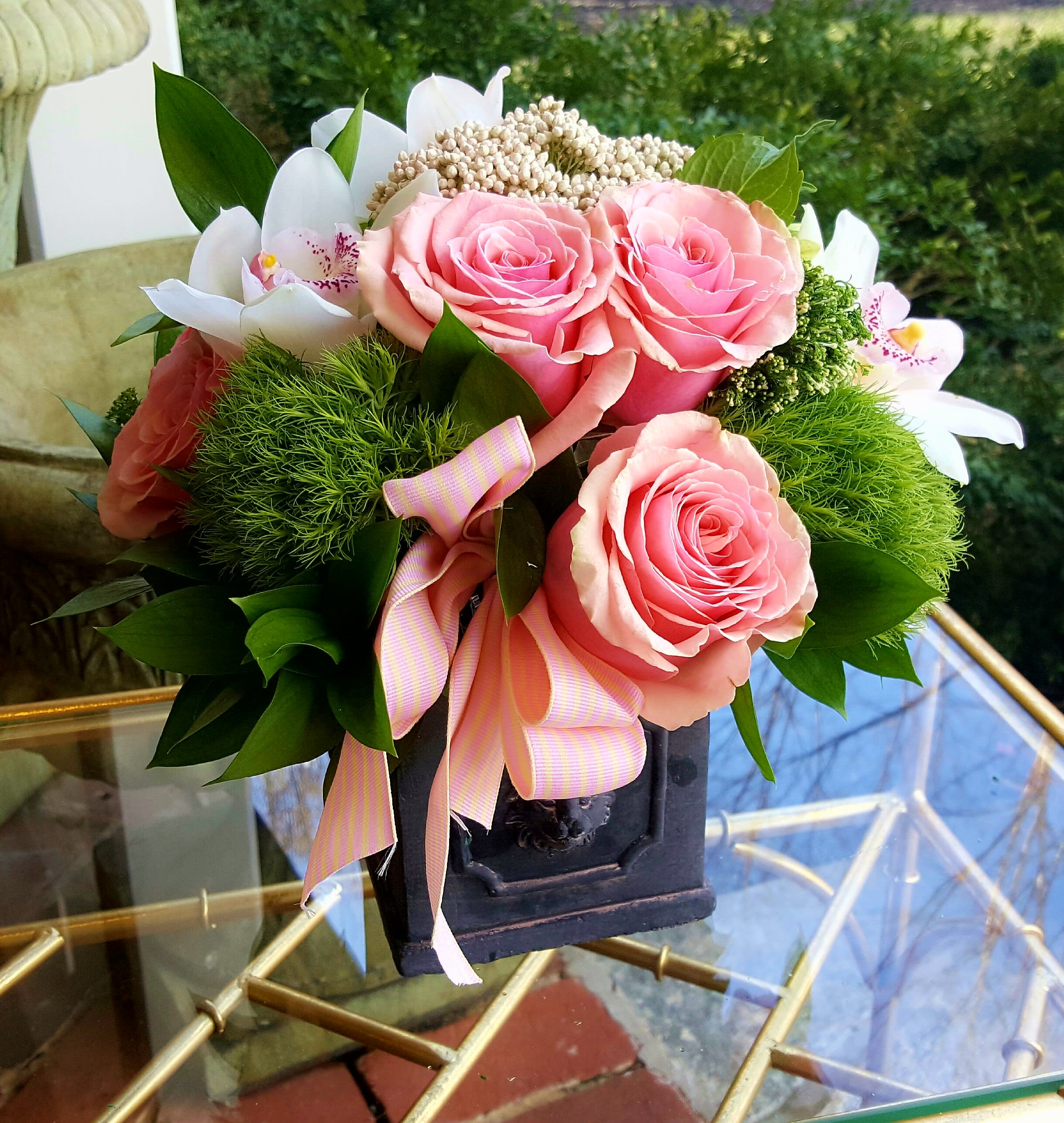 Pink roses and white orchids arranged in a dark vase with a striped ribbon