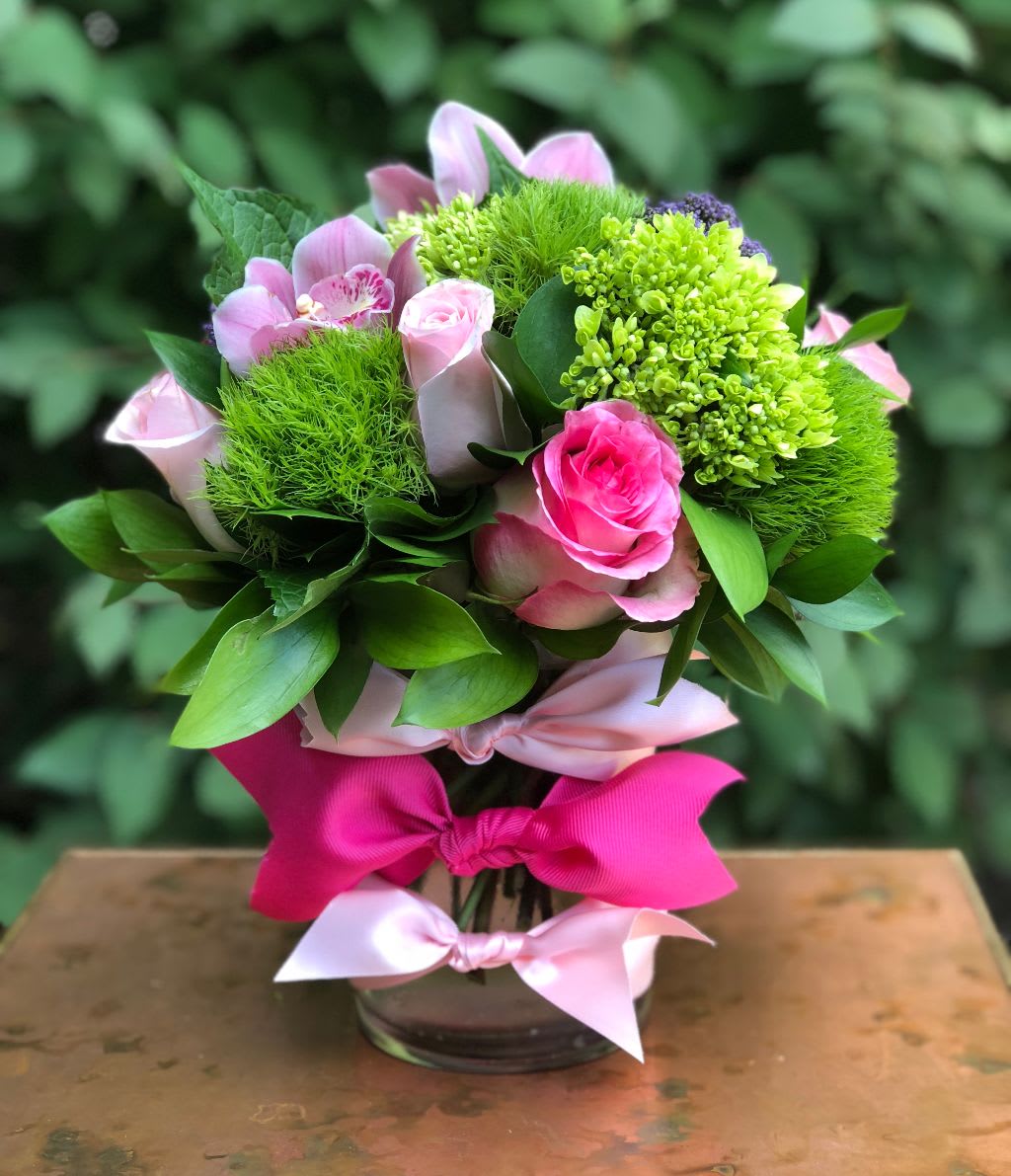 Pink roses and green blooms arranged in a glass vase with ribbon bows