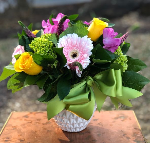 Bouquet of yellow roses, pink gerbera daisies, and purple flowers in a white vase
