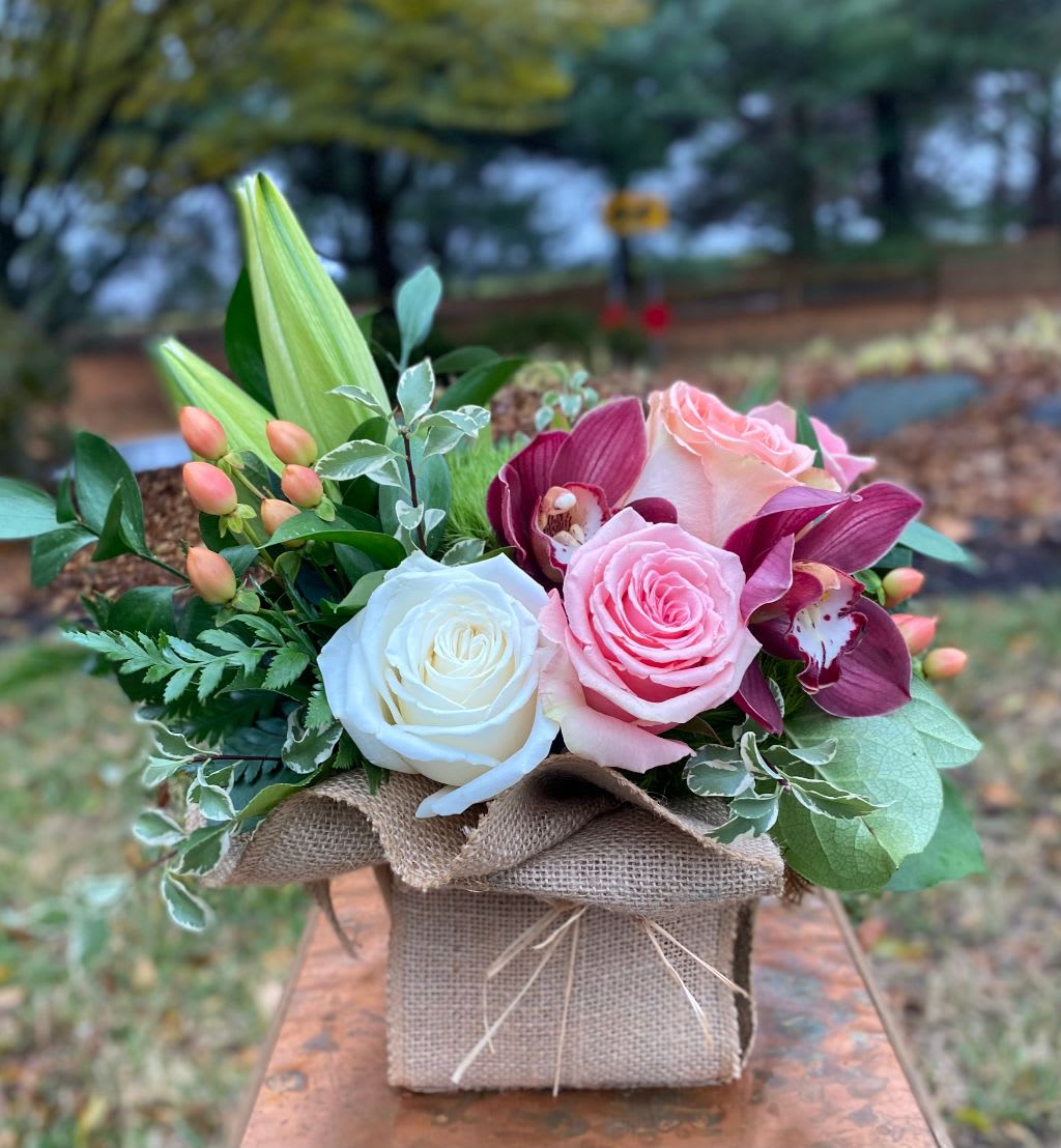 Pink and white roses with purple orchids in a burlap-wrapped box