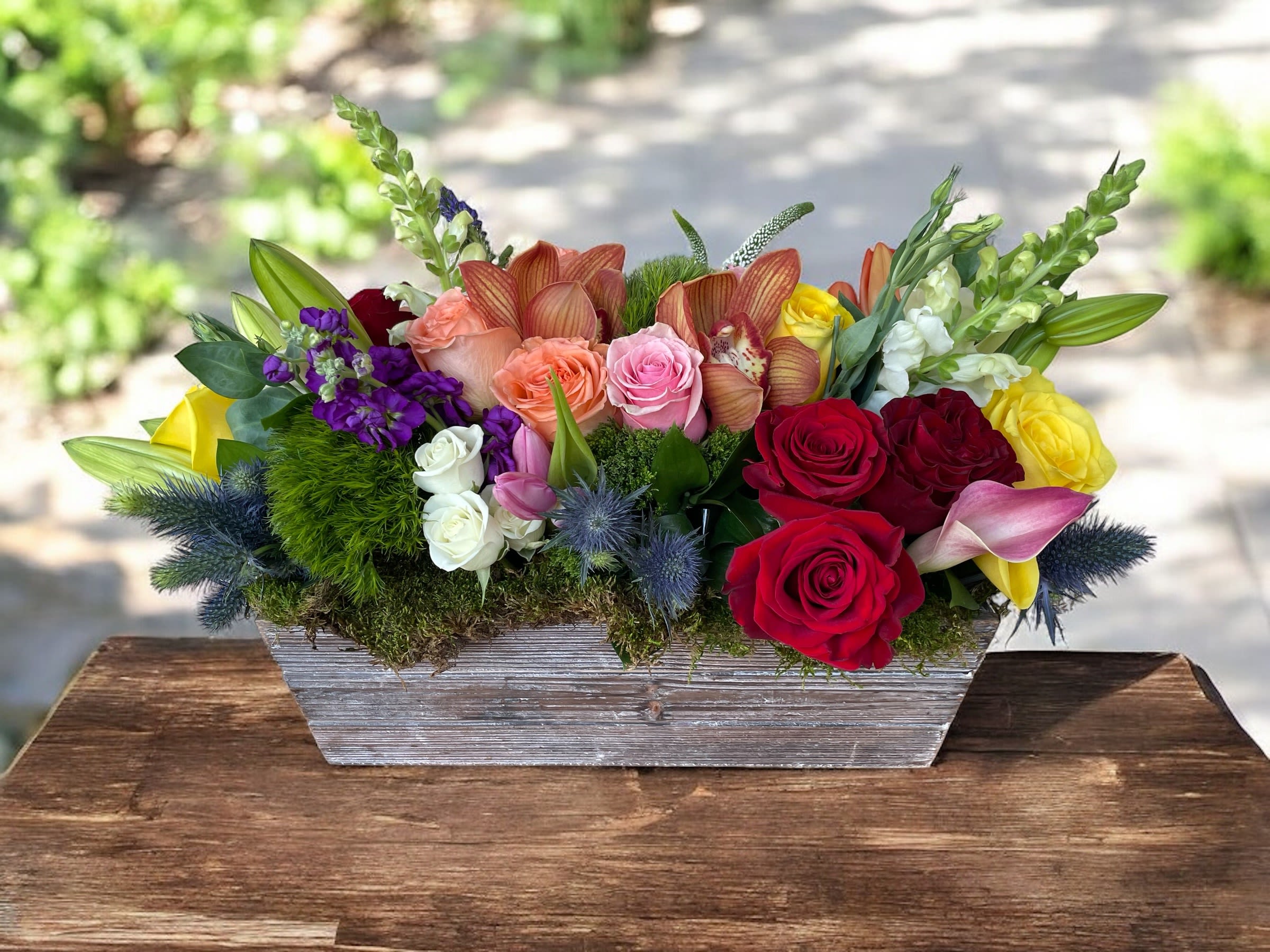 Mixed bouquet of roses, orchids, lilies, and snapdragons in a wooden planter