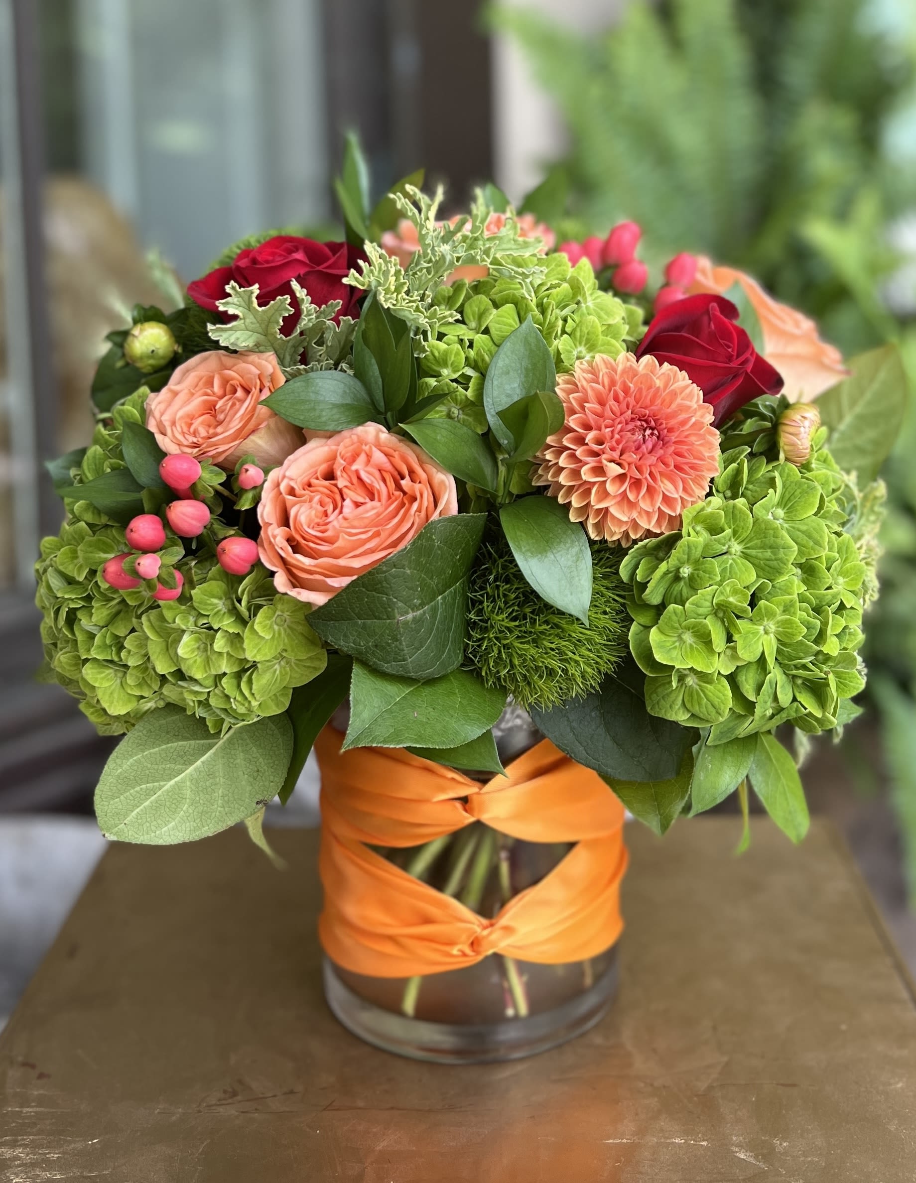 Bouquet of coral roses and green hydrangeas in a glass vase with orange ribbon