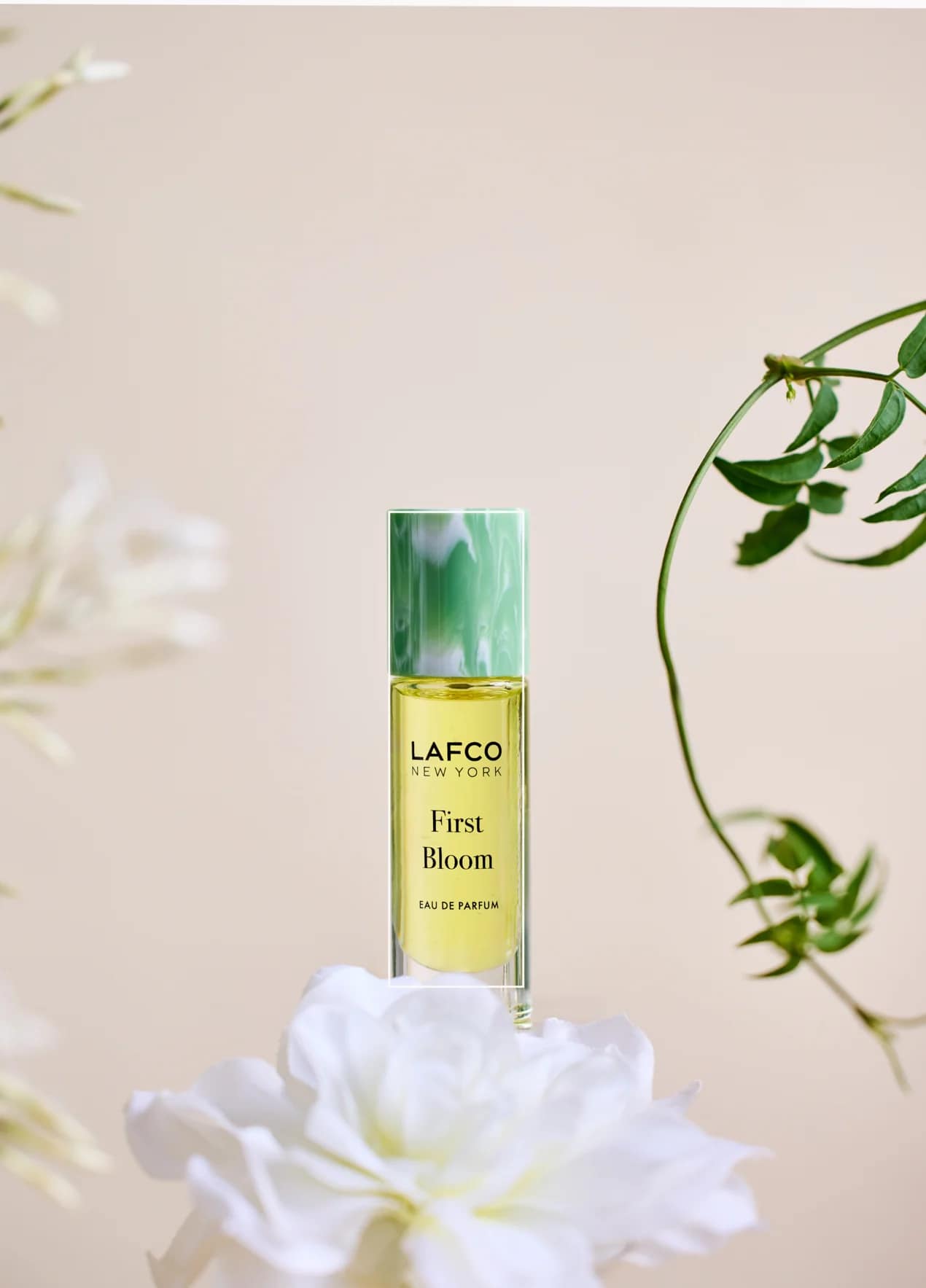A perfume bottle labeled LAFCO New York First Bloom with white flowers around it.