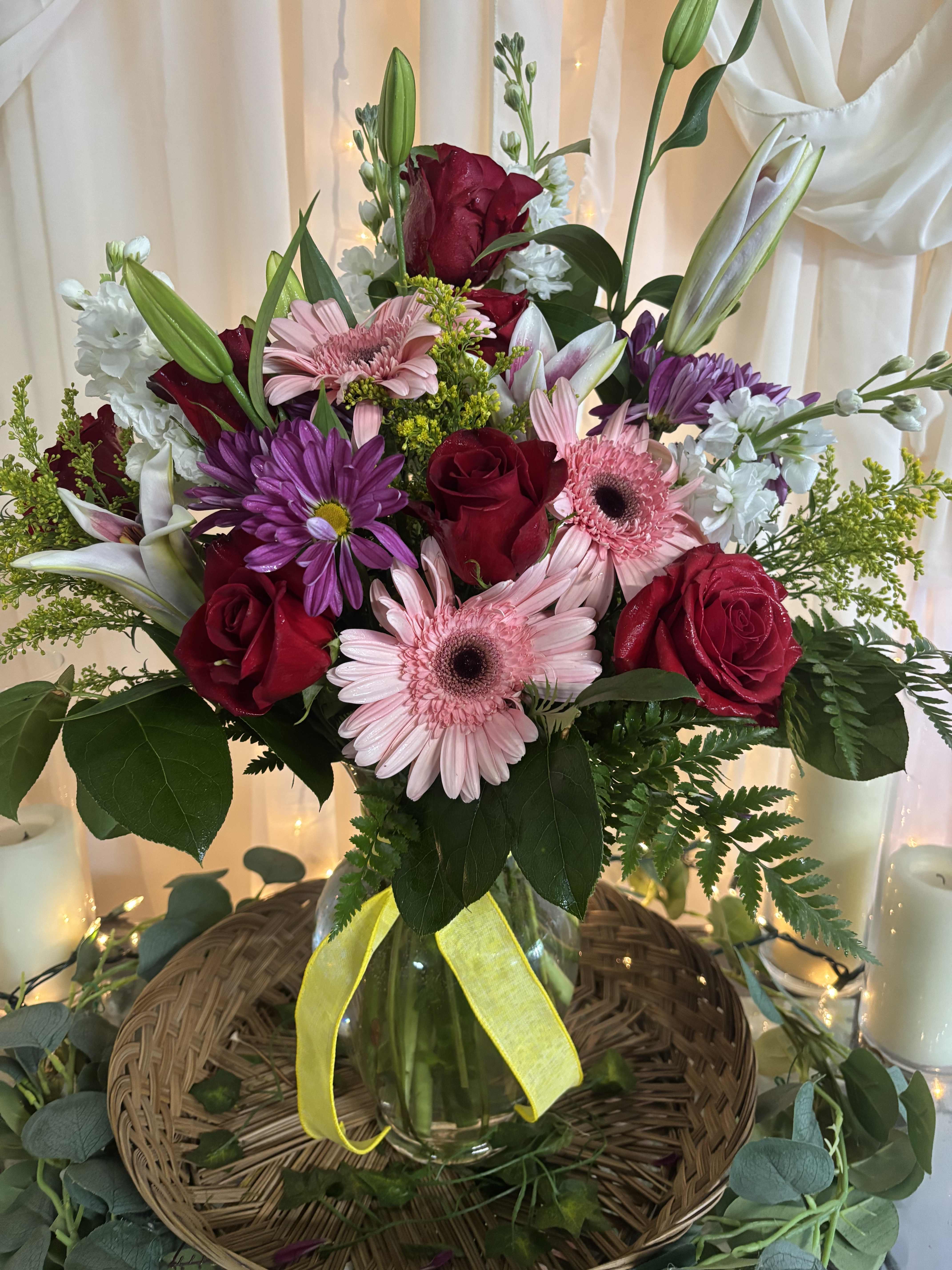 Mixed bouquet of roses, gerbera daisies, lilies, and purple daisies in a glass vase
