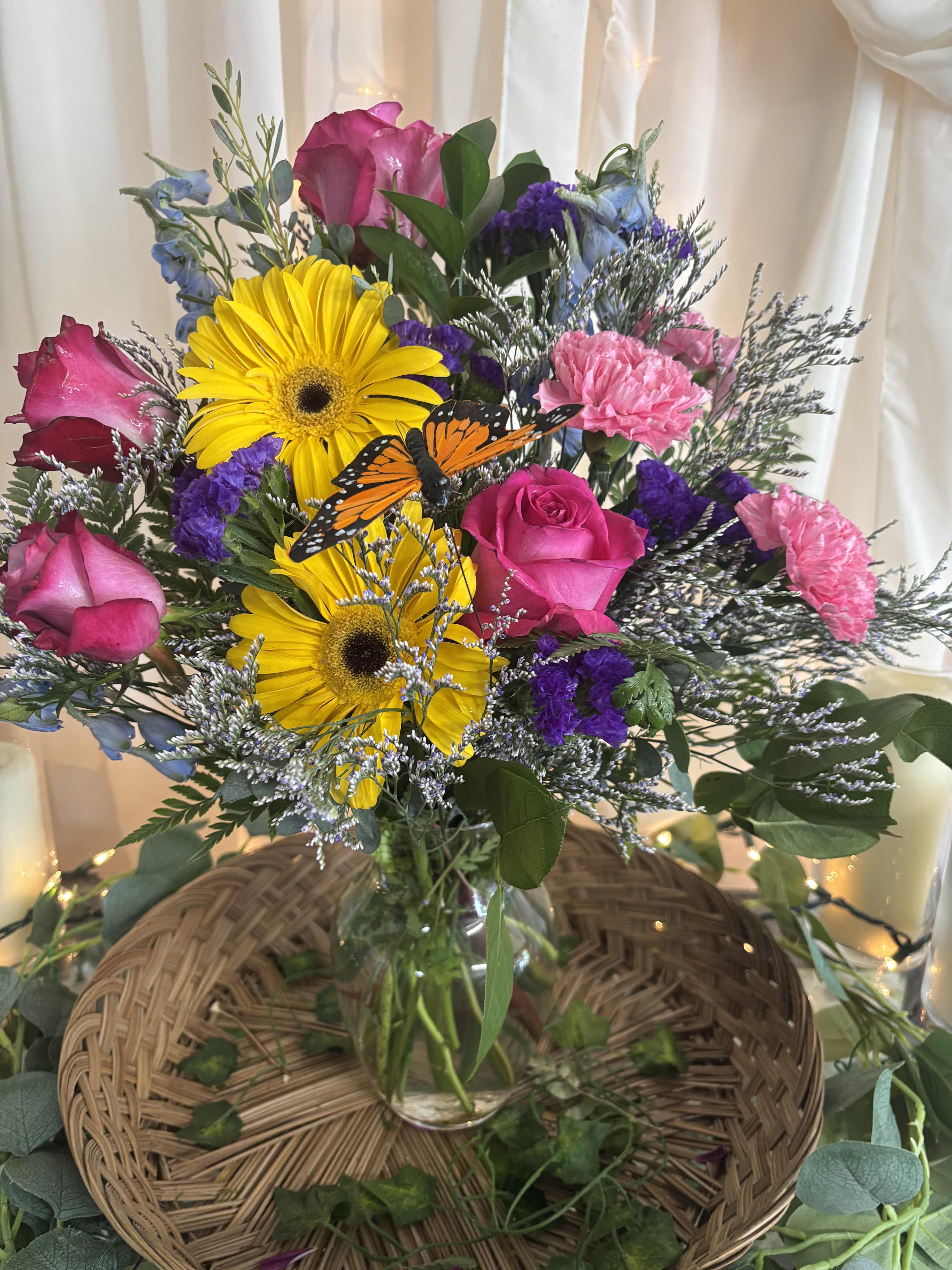Bouquet of pink roses, yellow gerbera daisies, and purple flowers in a glass vase