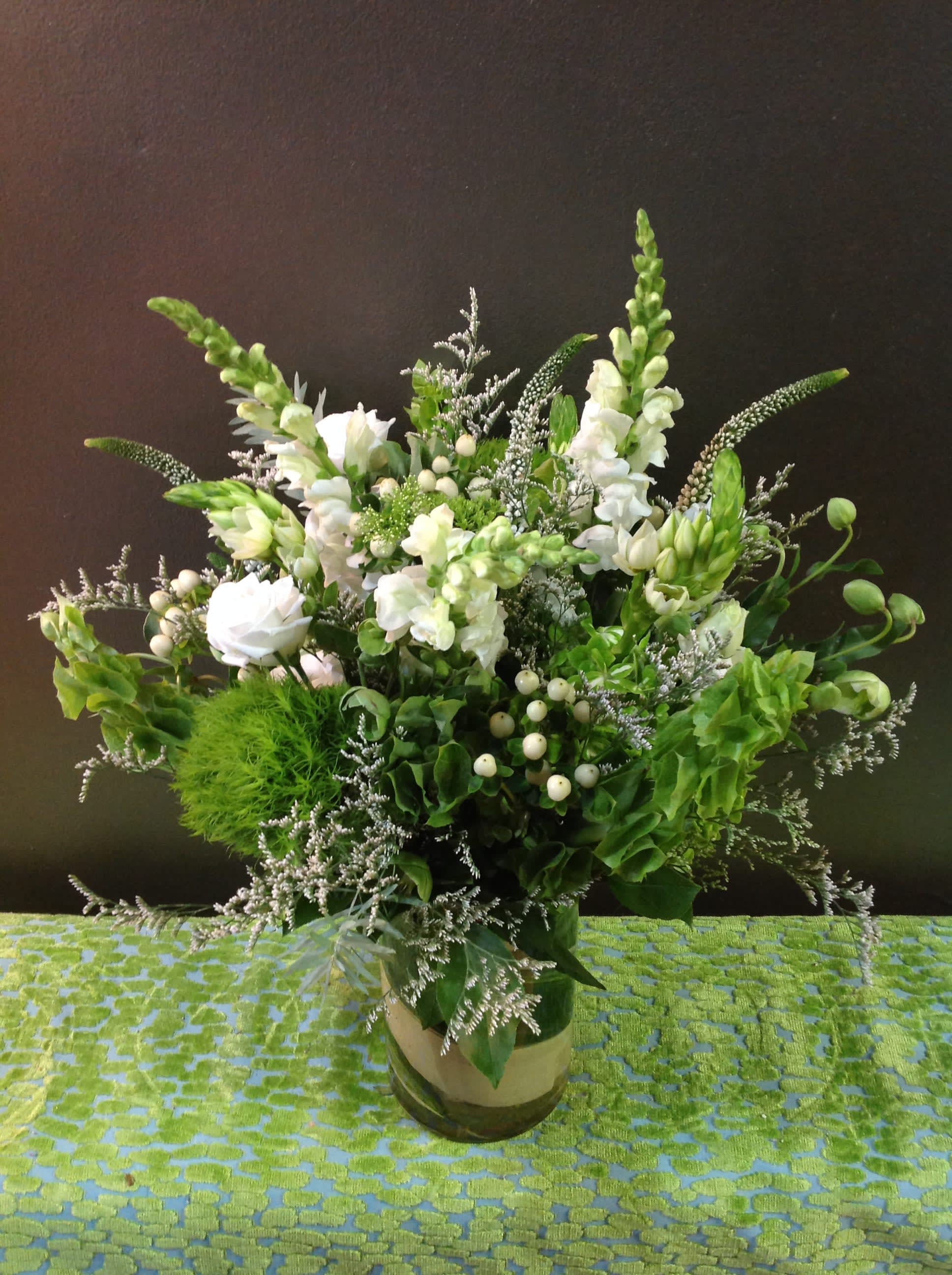 Tall green and white floral arrangement with snapdragons and roses in a clear glass cylinder vase