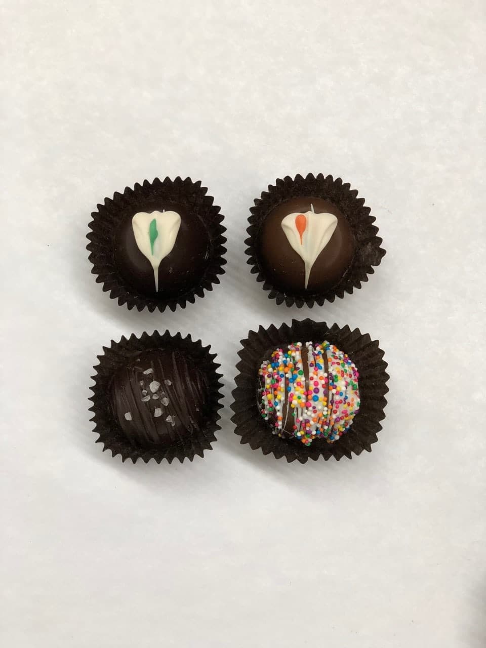 Four decorated chocolate truffles in dark paper cups on a white background