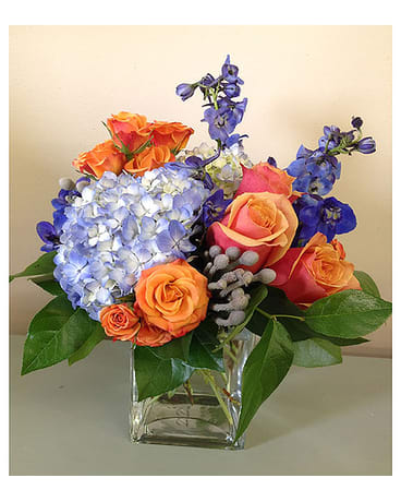 Bouquet of orange roses, blue hydrangea, and purple flowers in a glass vase