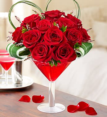 Red roses arranged in a martini glass with green ribbon accents