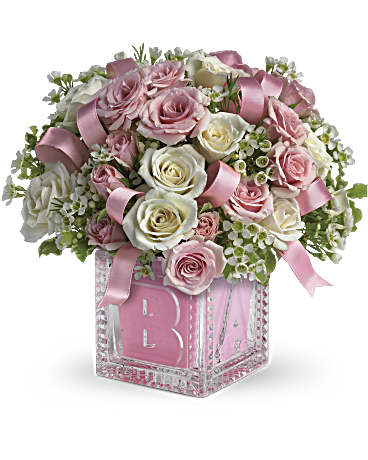 Pink and white roses arranged in a glass cube vase with a pink ribbon