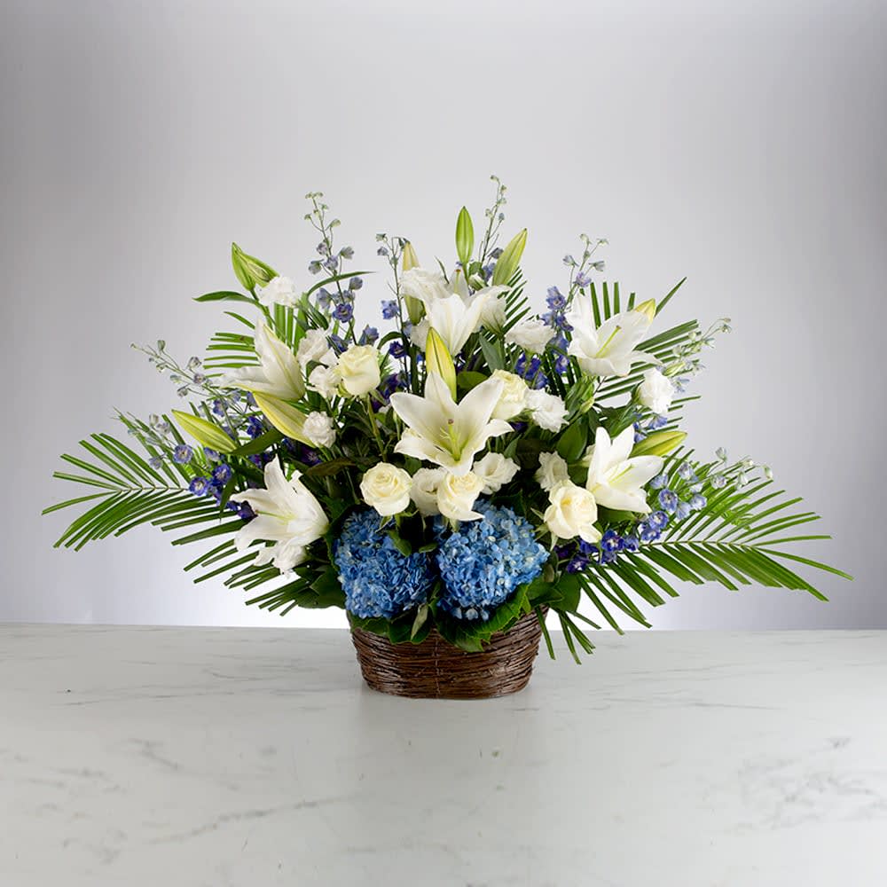 White lilies and blue hydrangeas in a woven basket arrangement