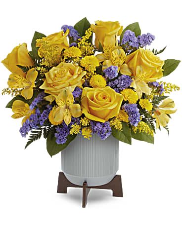 Yellow roses and purple filler flowers arranged in a white vase