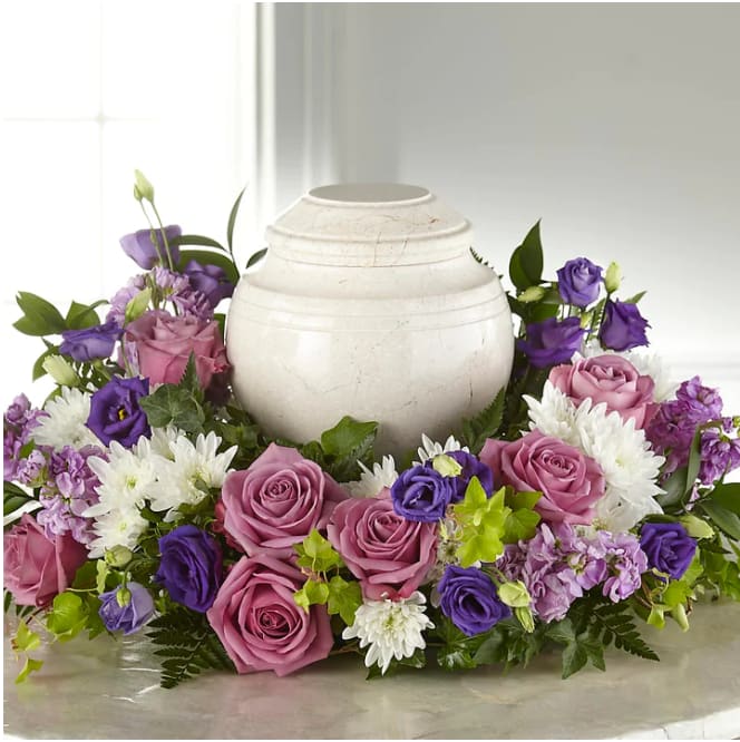 Purple and pink roses arranged around a white urn