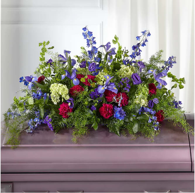 Large floral casket spray with blue, purple, pink, and white flowers