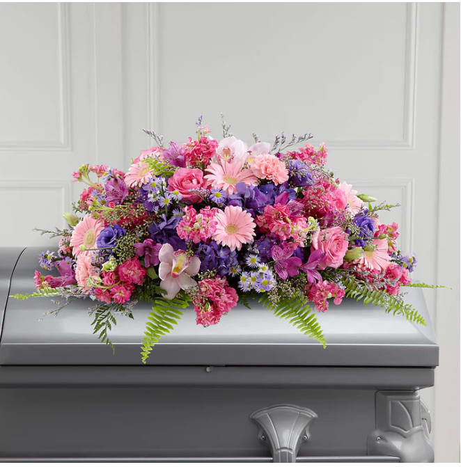Pink and purple floral casket spray on a gray casket