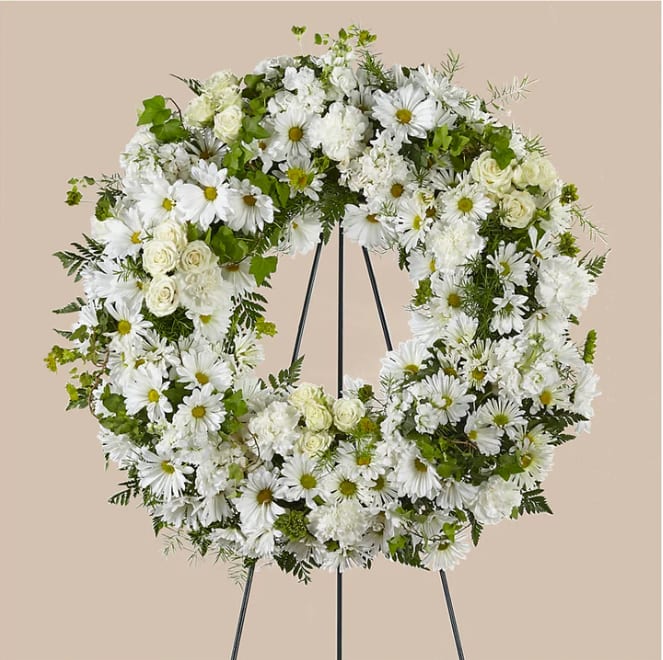 White floral wreath on a black stand with daisies and roses