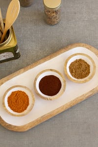 Wooden tray with three small bowls of spices and wooden spoons