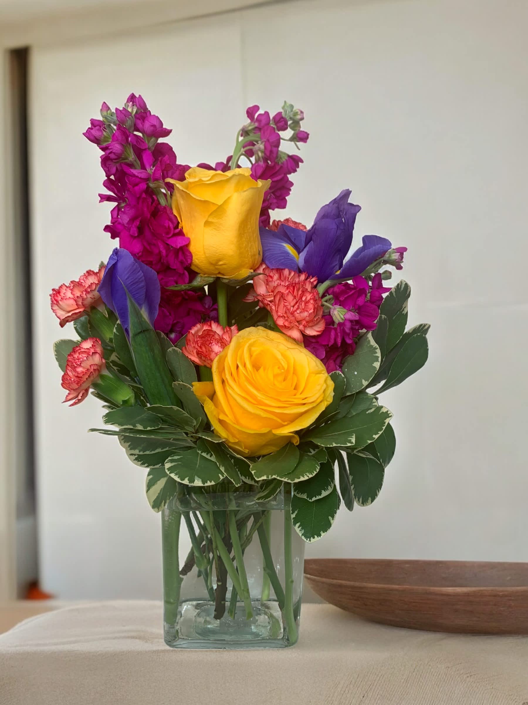 Colorful bouquet of yellow roses, purple irises, and pink flowers in a glass vase