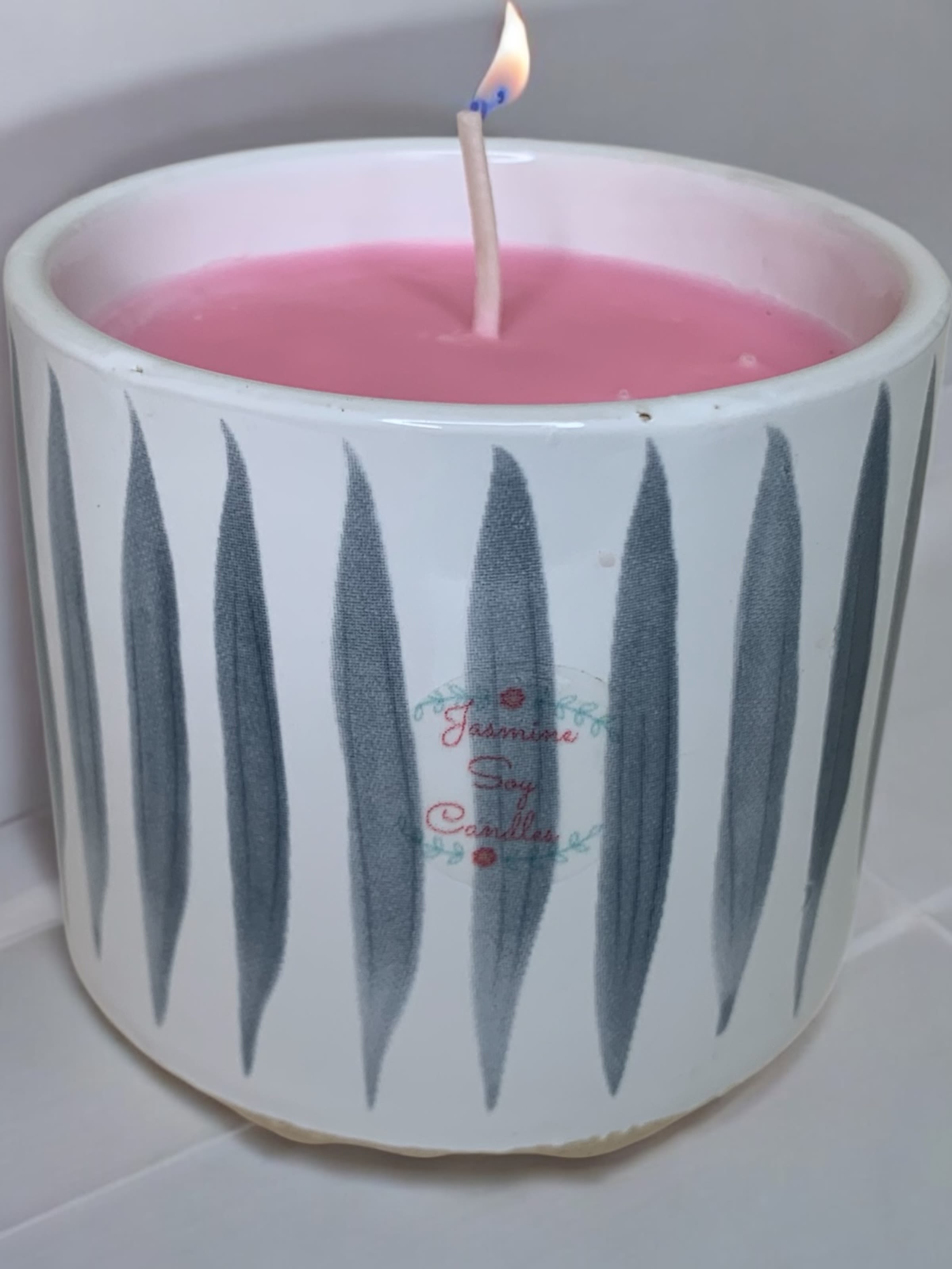 Pink candle in a white ceramic holder with a lit wick