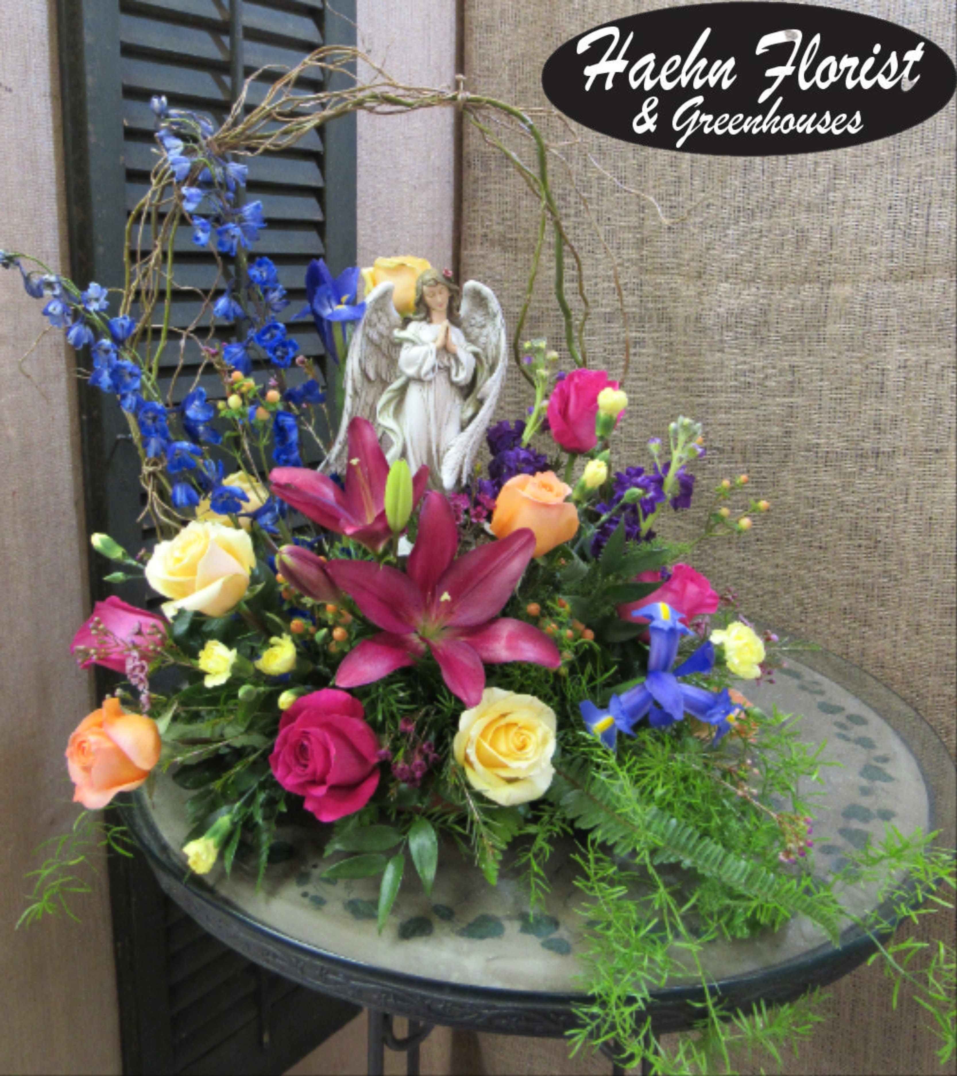 Colorful floral arrangement with roses, lilies, and an angel figurine
