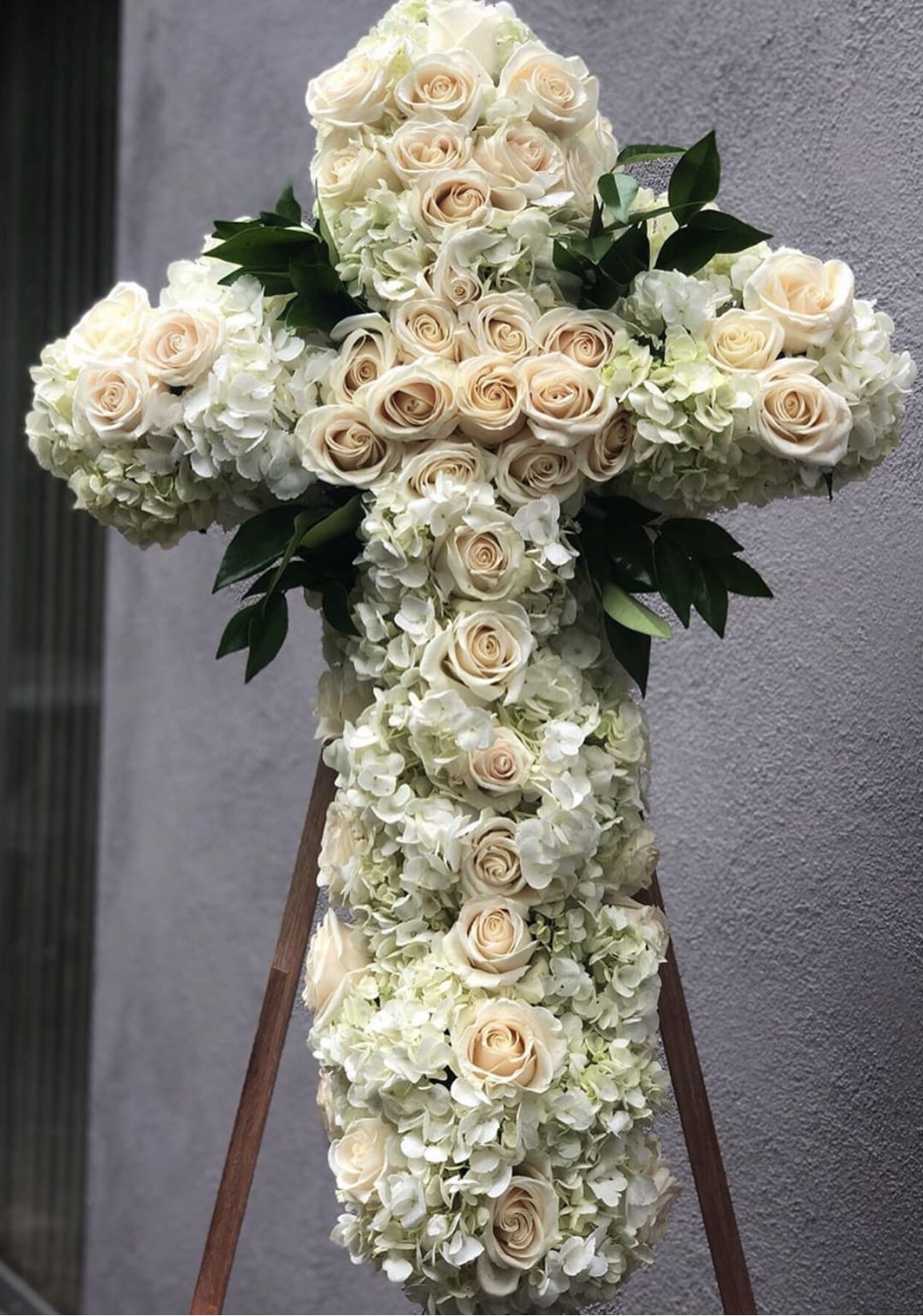 White floral cross with cream roses and hydrangeas on a stand