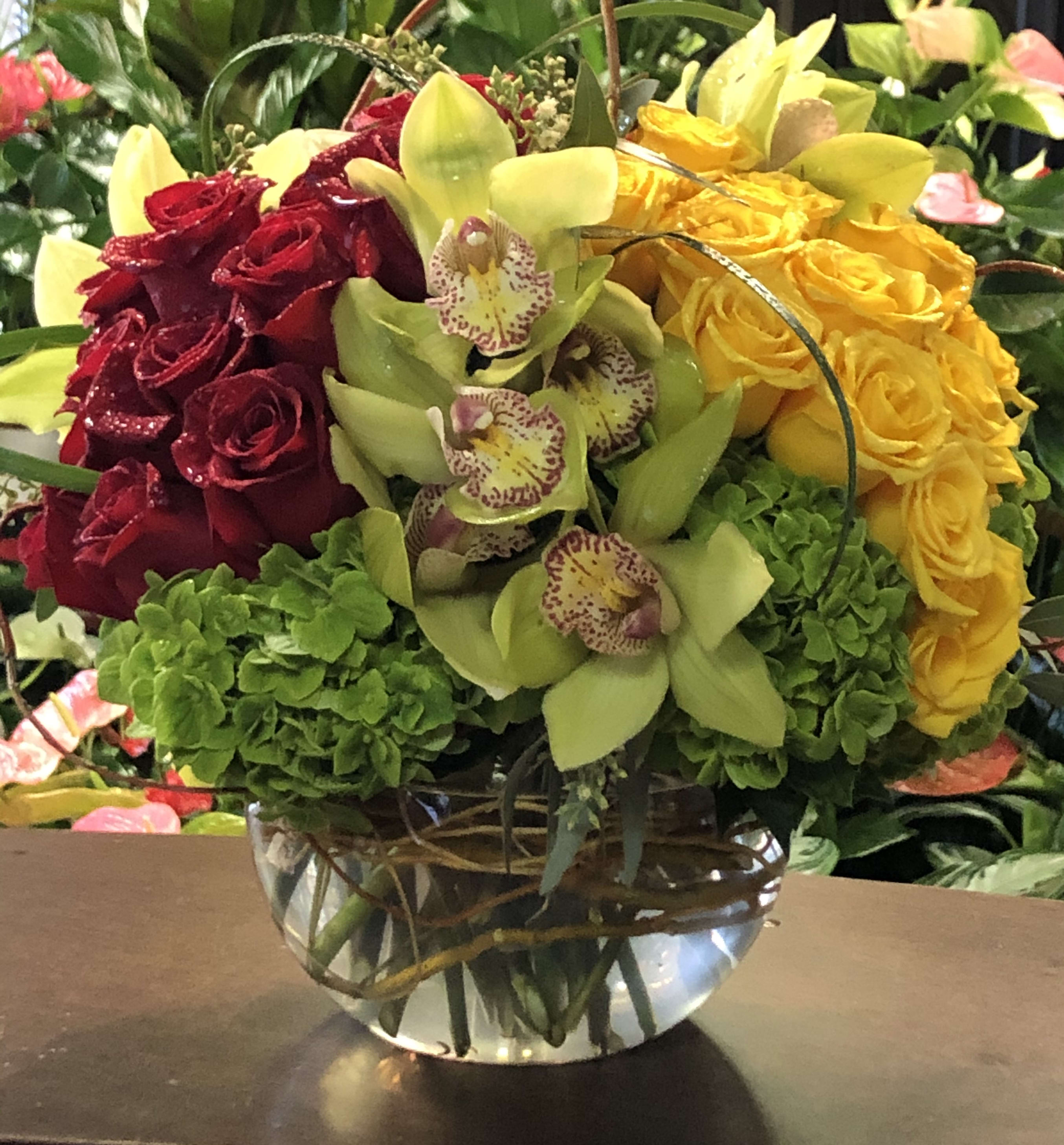 Bouquet of red and yellow roses with green orchids in a glass vase