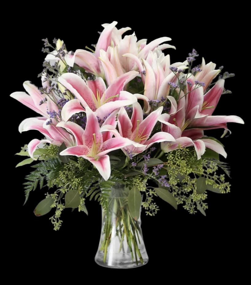 Pink lilies in a clear glass vase with purple filler flowers