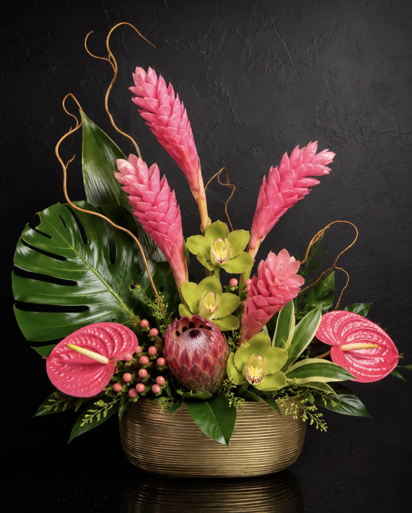 Tropical arrangement with pink blooms and green orchids in a gold vase