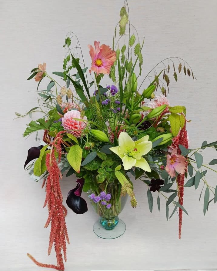 Tall garden-style arrangement with pink dahlias, green lily, dark calla lilies in a clear glass vase