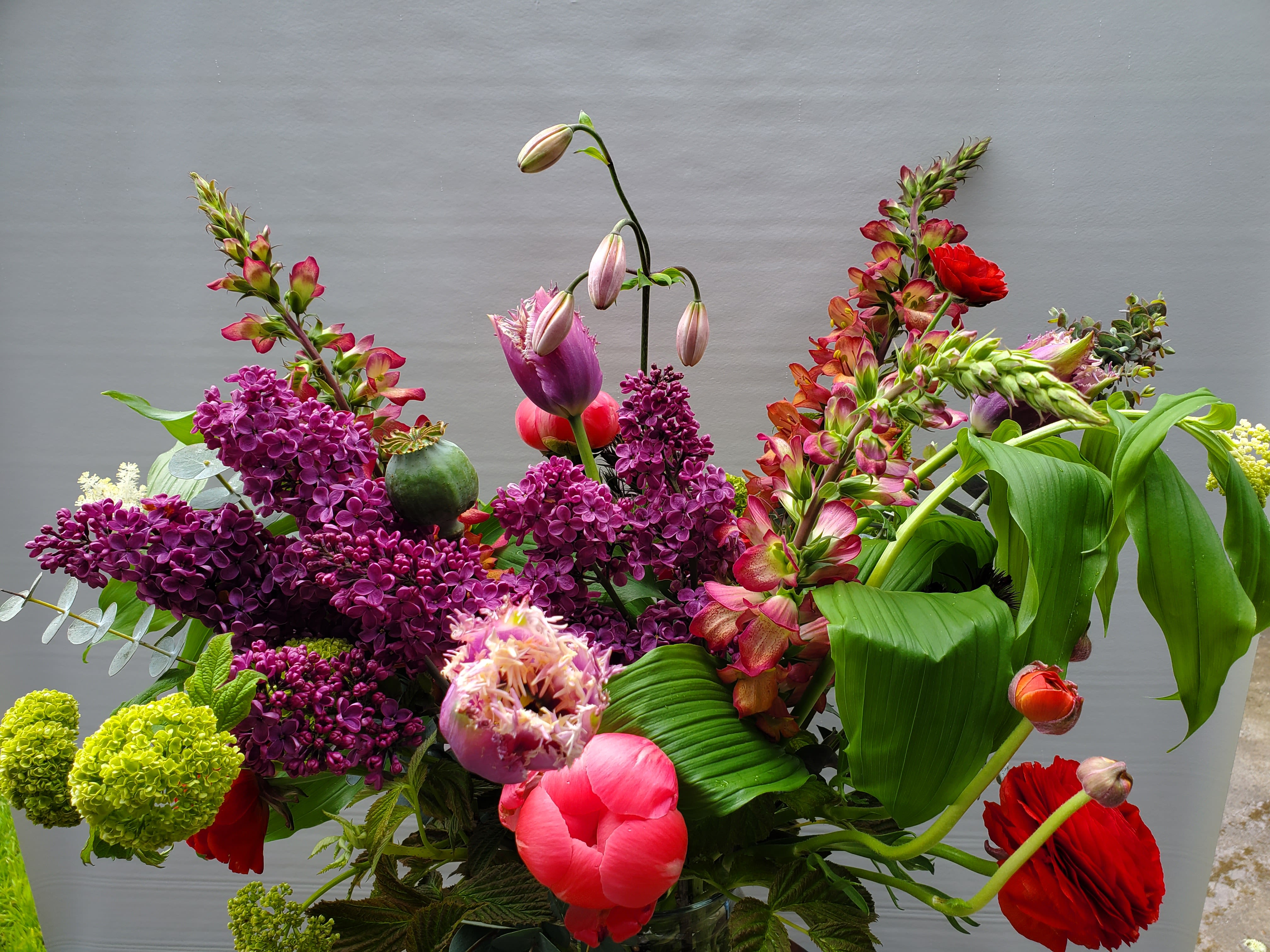 Tall mixed arrangement with purple lilacs, pink fringe tulips, and red blooms in a glass vase.