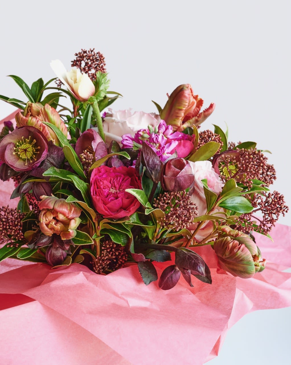 Hand-tied bouquet of pink and burgundy blooms wrapped in pink tissue paper.