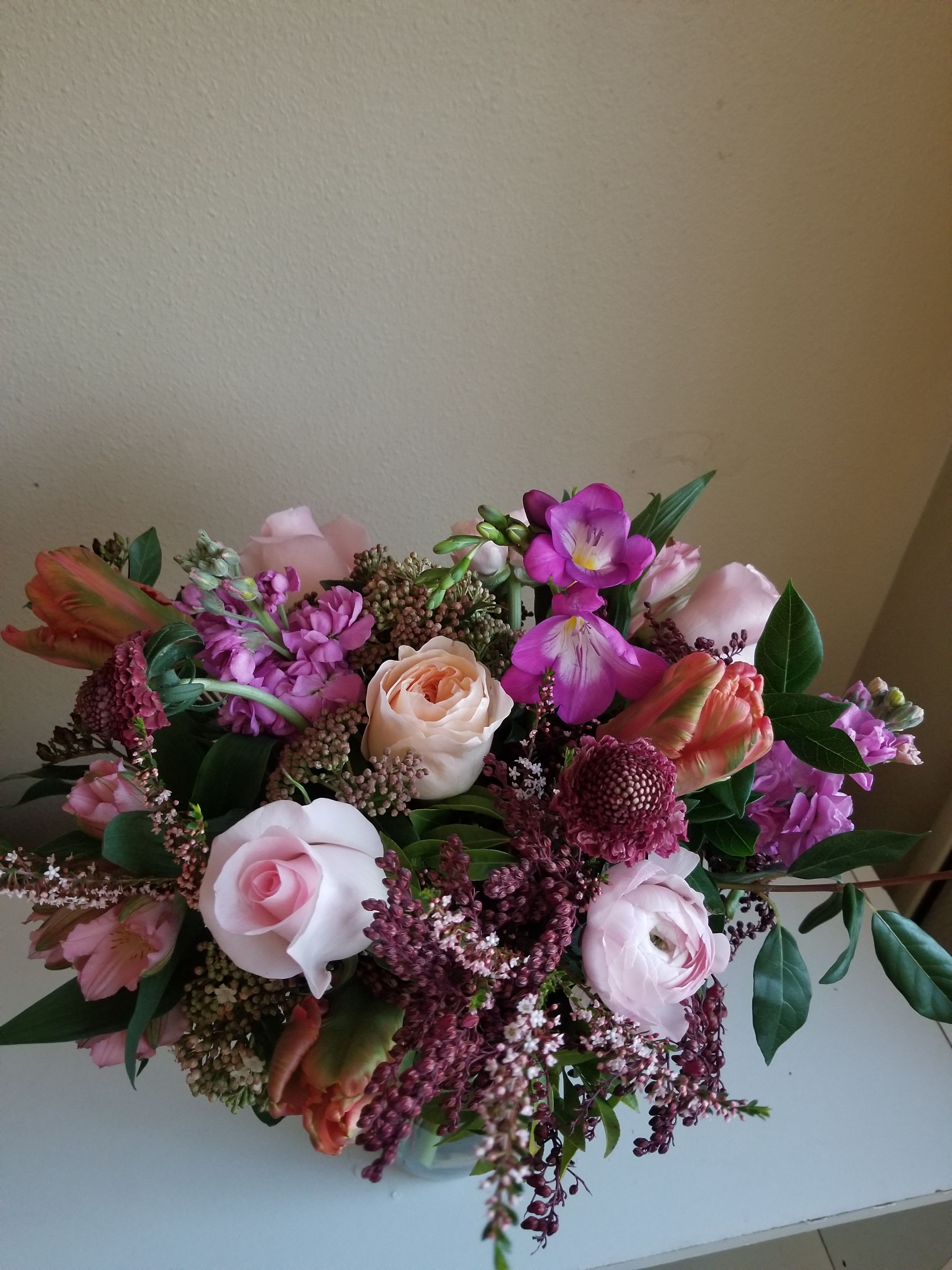Low pink and purple flower arrangement with roses and tulips in a clear glass vase