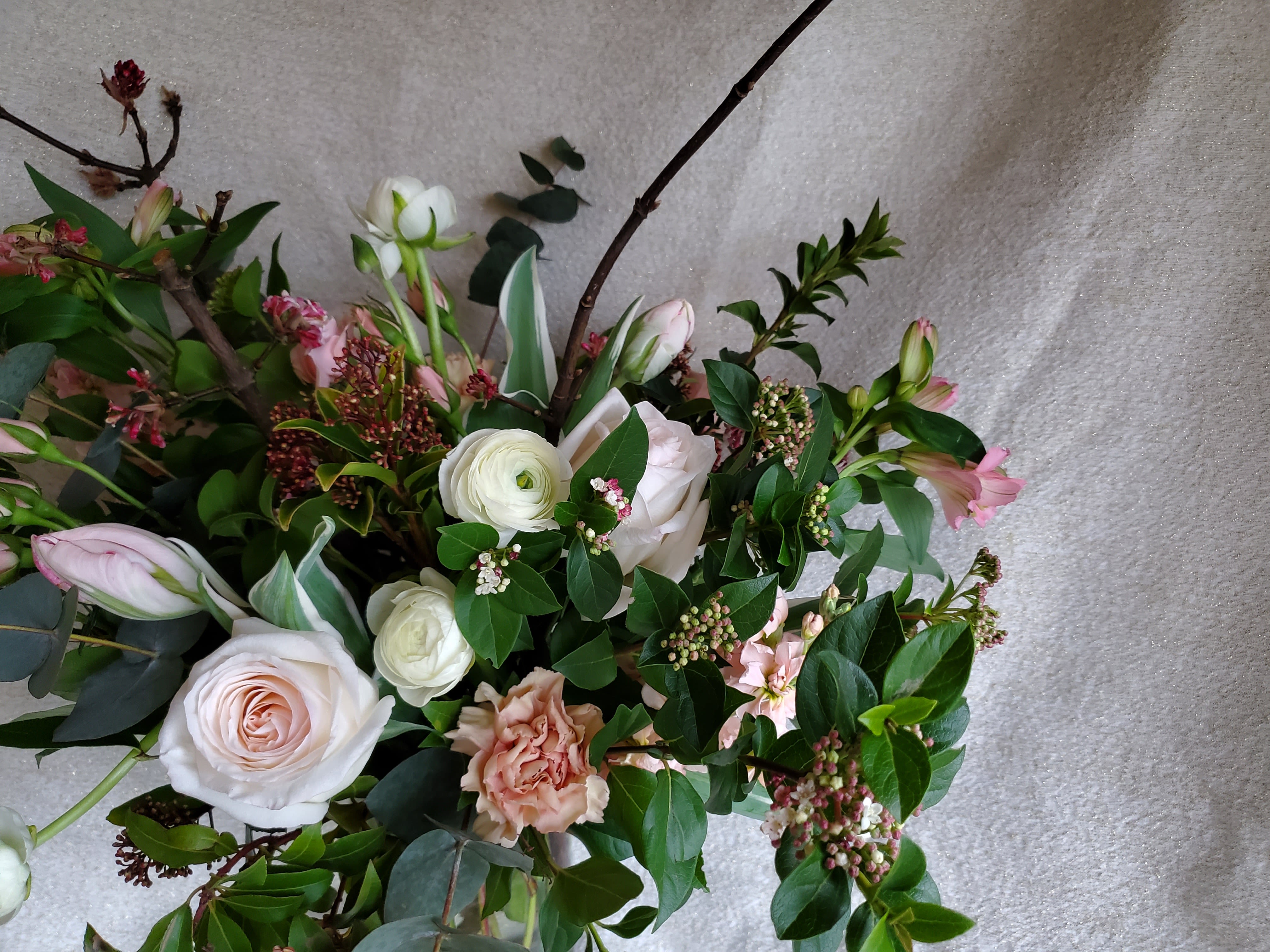 Loose arrangement of blush roses, white ranunculus, and pink flowers with branching accents