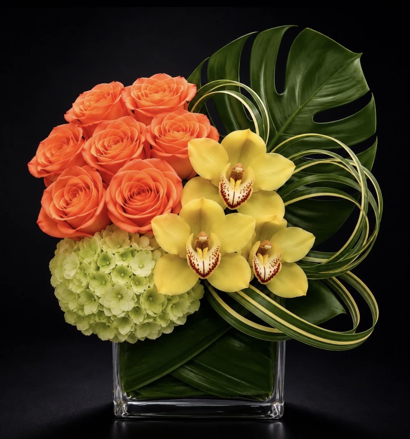 Orange roses, yellow orchids, and green hydrangea in a clear square vase