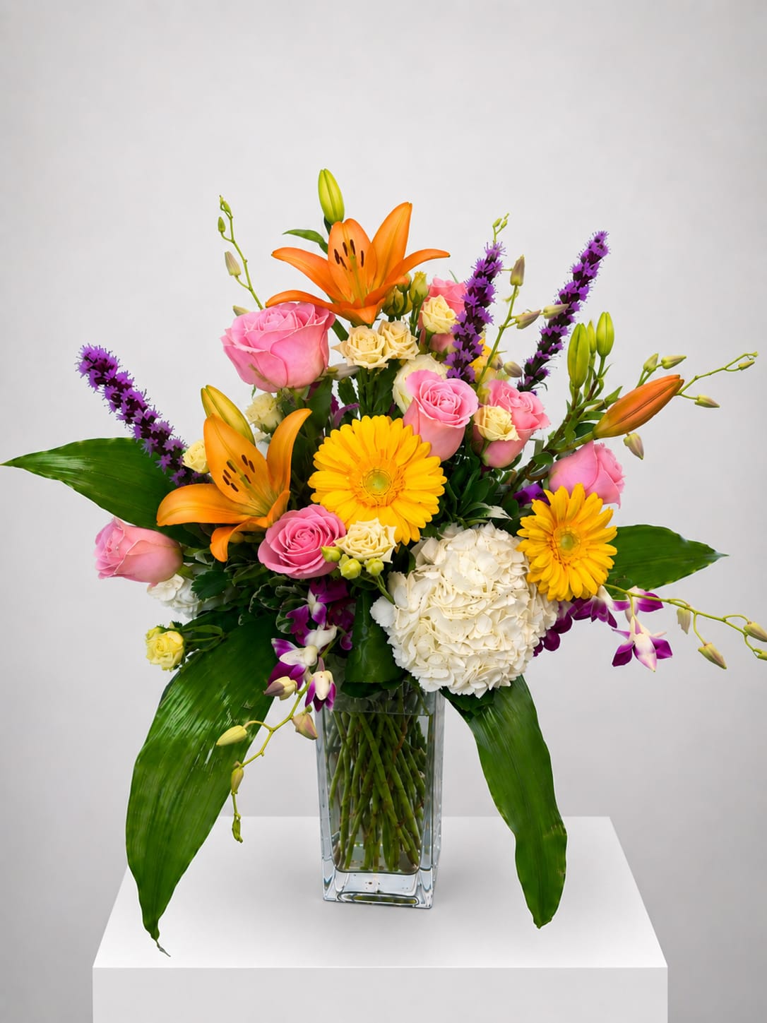 Mixed bouquet of orange lilies, pink roses, and yellow daisies in a glass vase