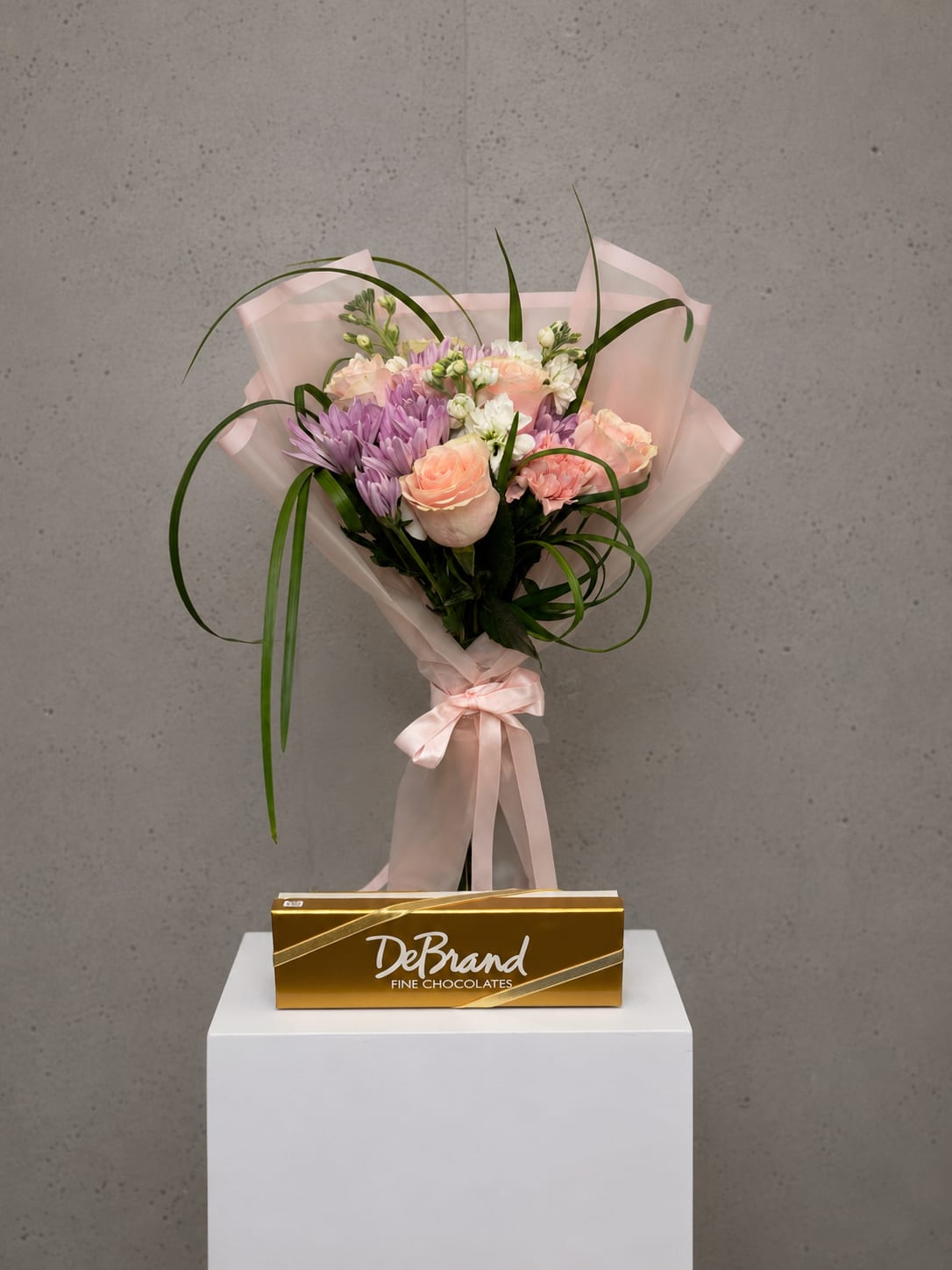 Sugar Bloom Wrap - Sugar Bloom is a charming gift set that combines a hand-designed wrapped bouquet with premium DeBrand Fine Chocolates for a thoughtful surprise that's perfect for birthdays, anniversaries, thank you gifts, get well wishes, thinking of you moments, or just because. Designed by the floral artists at All Occasions Florist in Dallas, TX, this bouquet features fresh seasonal flowers in soft pastel shades, including roses, chrysanthemums, carnations, stock, and premium greenery, all beautifully wrapped in elegant blush paper with a satin ribbon. Paired with gourmet chocolates, Sugar Bloom offers the perfect combination of fresh flowers and sweet treats with convenient same-day flower delivery throughout Dallas and surrounding communities.  Disclaimer: This is a wrapped bouquet and does not include a vase. To ensure maximum freshness, the bouquet must be placed in clean water immediately upon delivery. Because we cannot guarantee when the flowers will be placed in water after delivery, Sugar Bloom is not eligible for refunds or replacements due to freshness or longevity concerns. We recommend having a vase ready before your flowers arrive. 