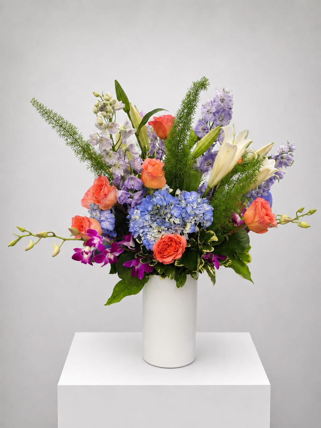 Colorful mixed bouquet in a white vase with roses, lilies, hydrangeas, and orchids