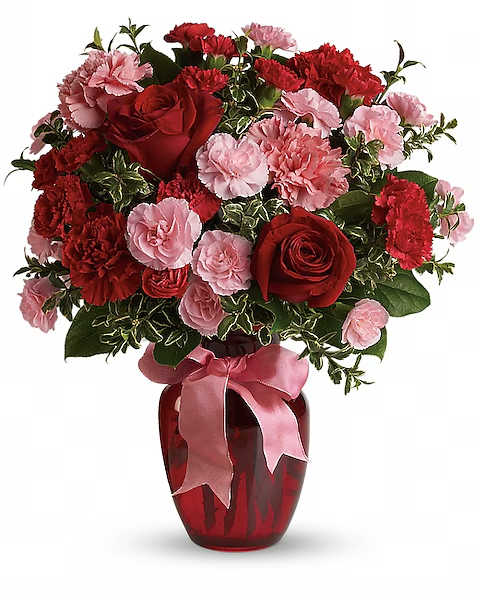 Red roses and pink carnations in a red glass vase with a pink ribbon