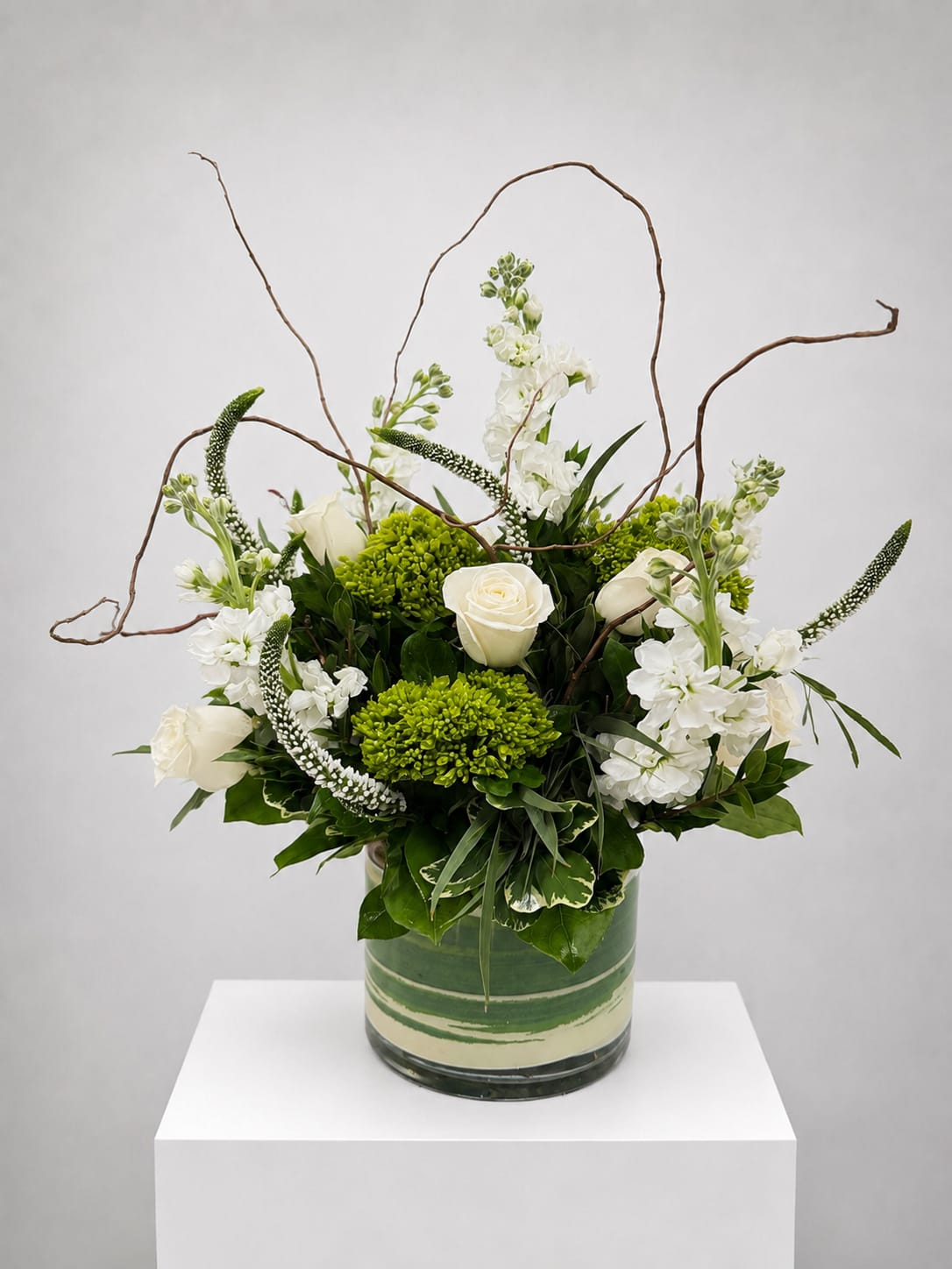 White roses and green blooms in a glass vase with curly branches