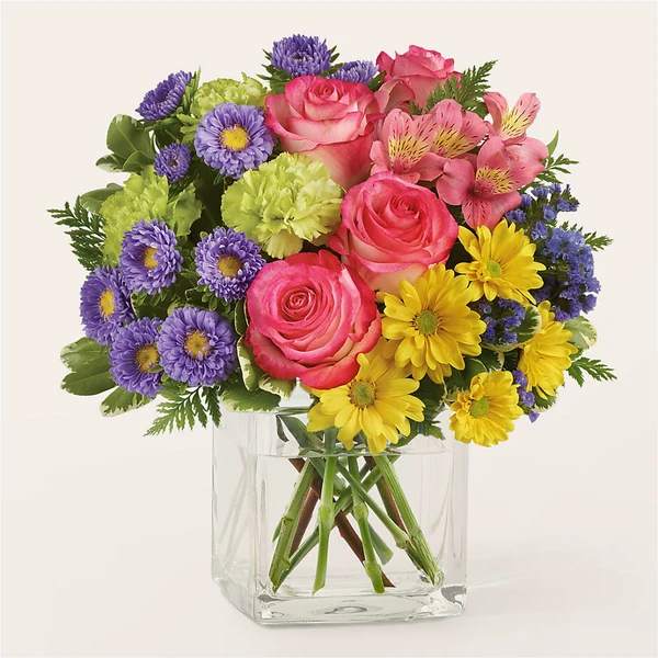 Bouquet of pink roses, purple daisies, and yellow flowers in a clear glass vase
