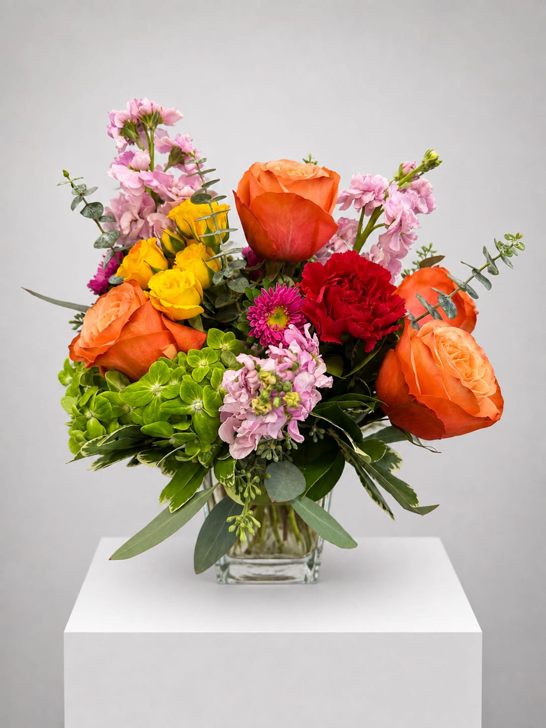 Mixed bouquet of orange and yellow roses with pink blooms in a glass vase