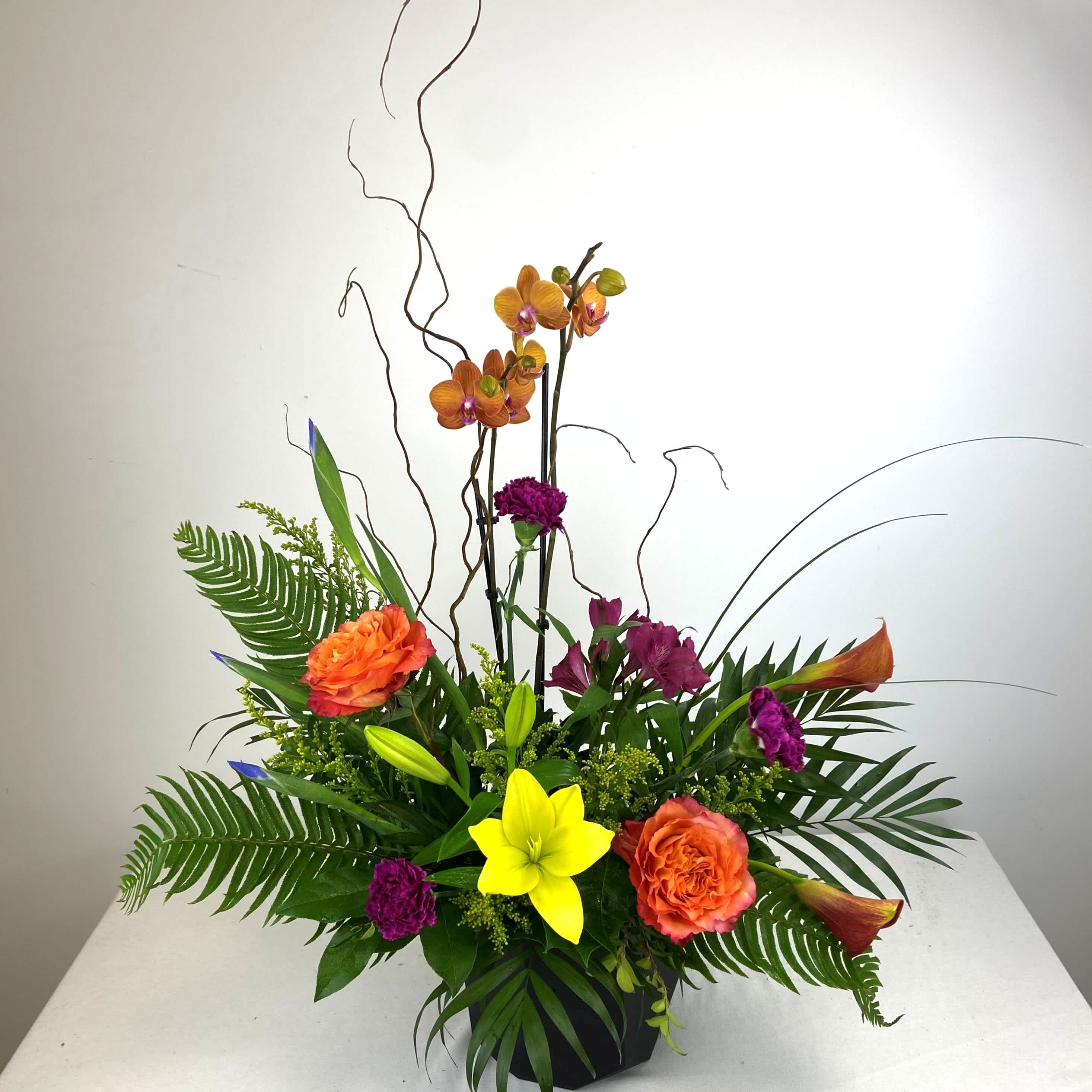 Tropical flower arrangement with orchids, lilies, and orange roses in a black vase