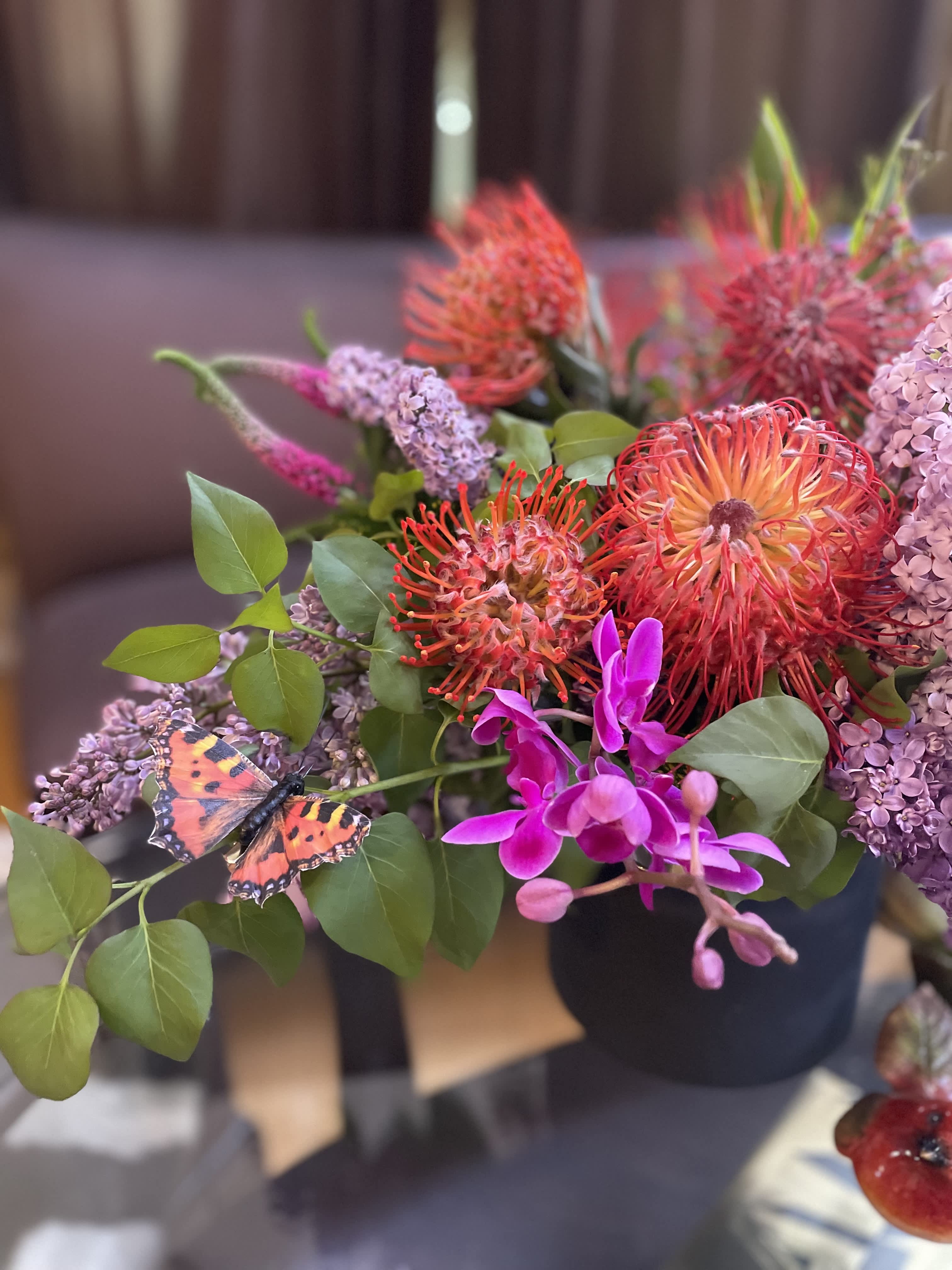 Bouquet of orange pincushion blooms and purple flowers with a butterfly accent